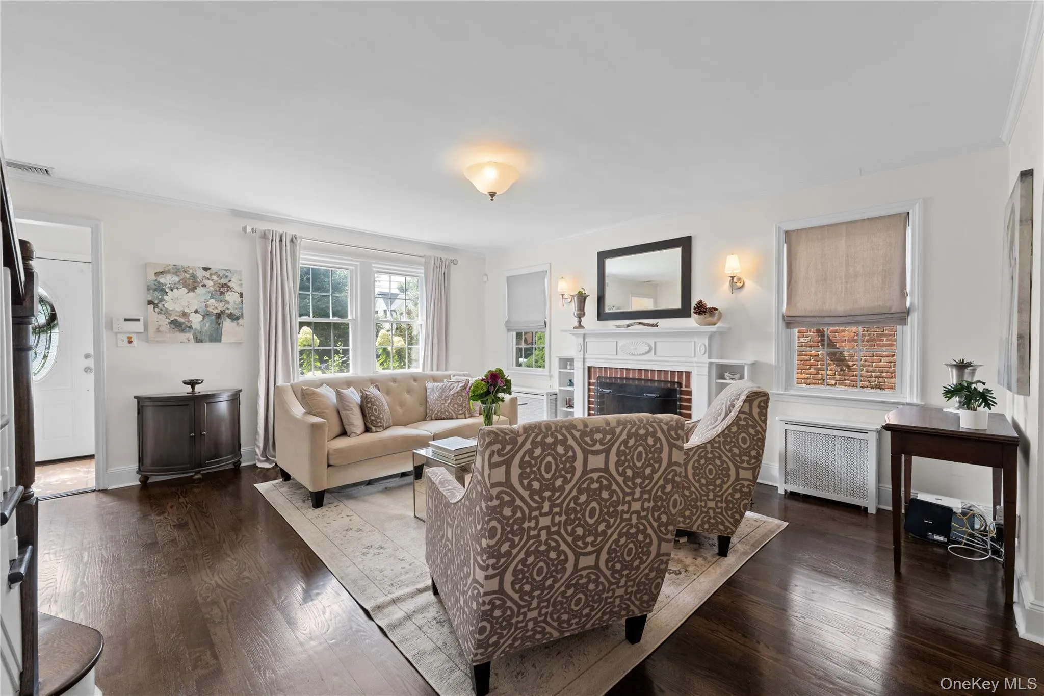 Hardwood flooring, fireplace with brick surround, built-in shelving, sconce lighting, and multiple windows Hardwood flooring, fireplace with brick surround, built-in shelving, sconce lighting, and multiple windows