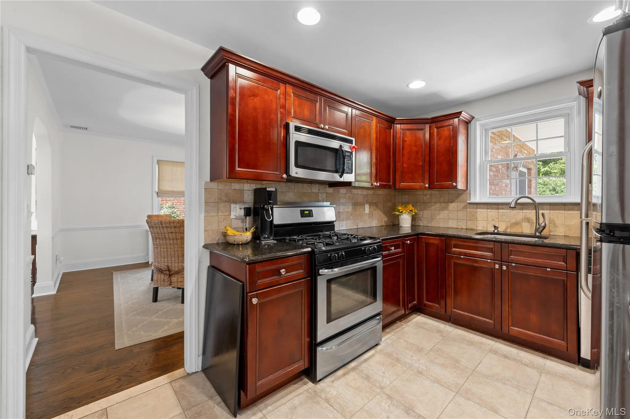 Kitchen featuring wood cabinetry, stainless steel appliances, granite countertops, and tiled flooring Kitchen featuring wood cabinetry, stainless steel appliances, granite countertops, and tiled flooring