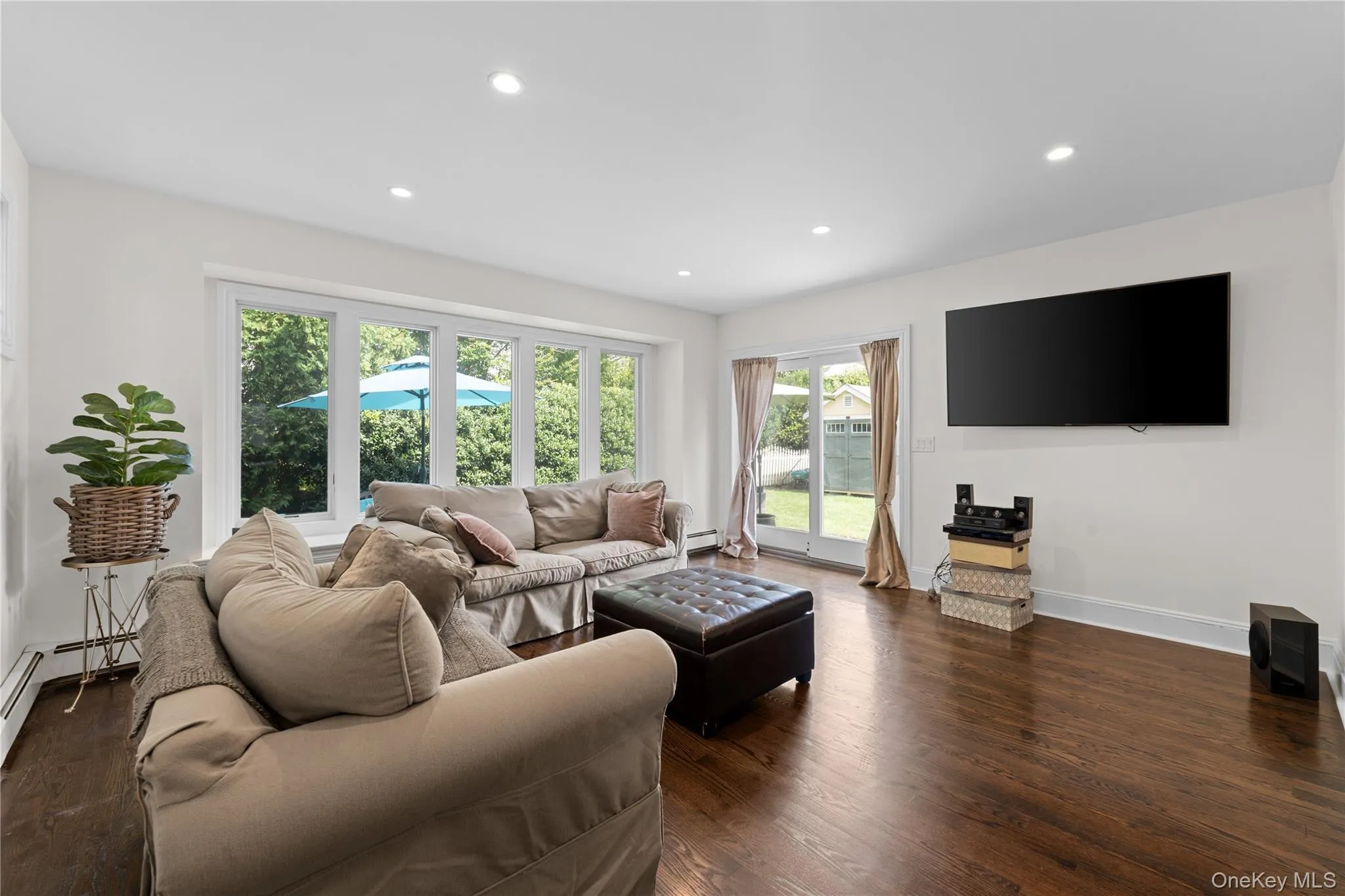 Recessed lighting illuminating dark wood-finish flooring, a multi-pane bay window, and a glass-paneled patio door leading to paver stone patio and large beautiful side yard with shed. Recessed lighting illuminating dark wood-finish flooring, a multi-pane bay window, and a glass-paneled patio door leading to paver stone patio and large beautiful side yard with shed.