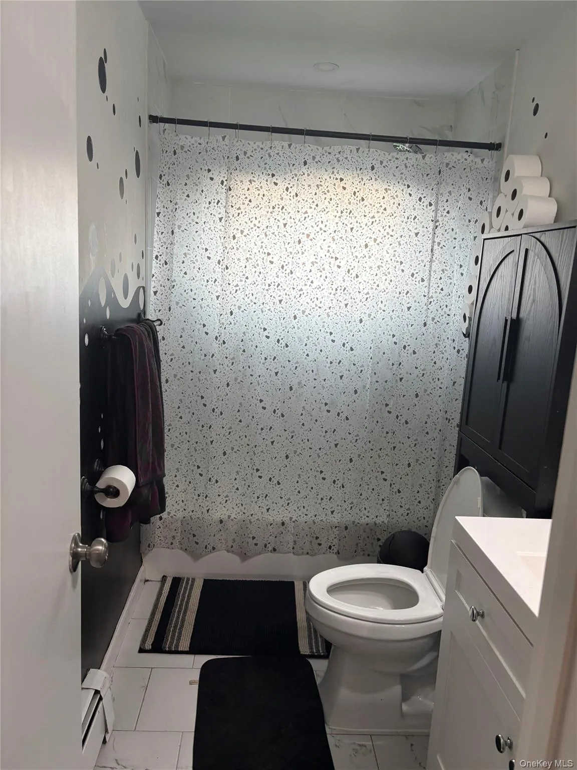 Tiled bathroom featuring a white vanity with a rectangular sink, a toilet, a built-in shower, and a dark wood-finish cabinet Tiled bathroom featuring a white vanity with a rectangular sink, a toilet, a built-in shower, and a dark wood-finish cabinet