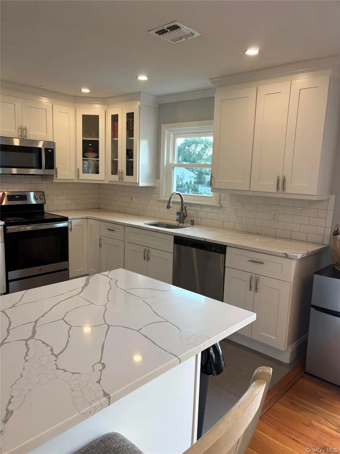 White shaker-style cabinetry, stainless steel appliances, light-toned countertops with distinctive veining, subway tile backsplash, and recessed lighting White shaker-style cabinetry, stainless steel appliances, light-toned countertops with distinctive veining, subway tile backsplash, and recessed lighting