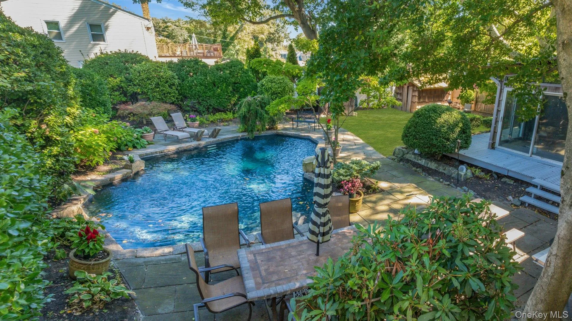 Private backyard oasis featuring a freeform swimming pool with stone coping, a stone patio, and mature landscaping Private backyard oasis featuring a freeform swimming pool with stone coping, a stone patio, and mature landscaping