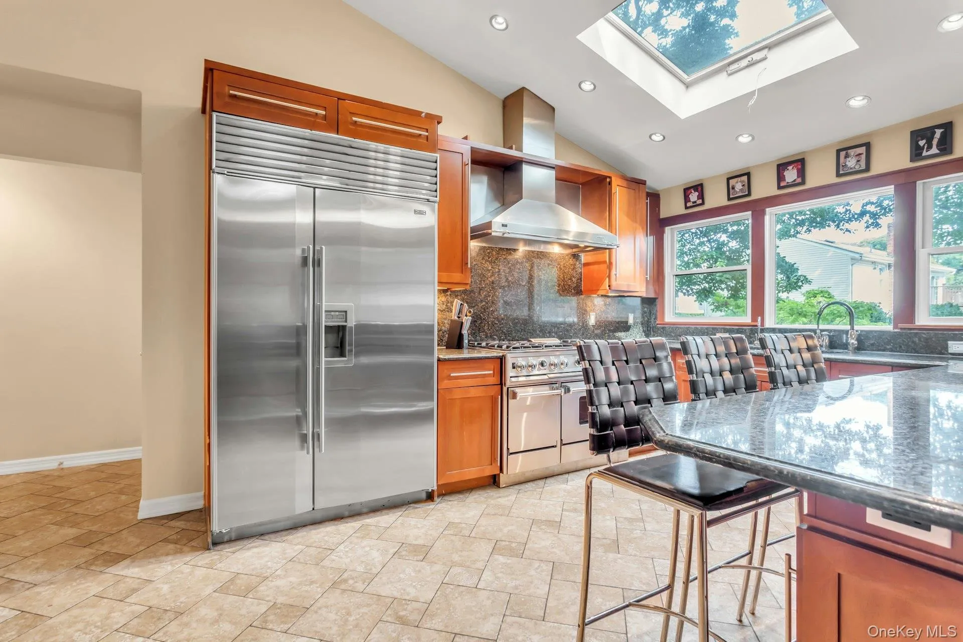 Stainless steel refrigerator, wood cabinetry, stone-finish countertops, tile flooring, and a skylight Stainless steel refrigerator, wood cabinetry, stone-finish countertops, tile flooring, and a skylight