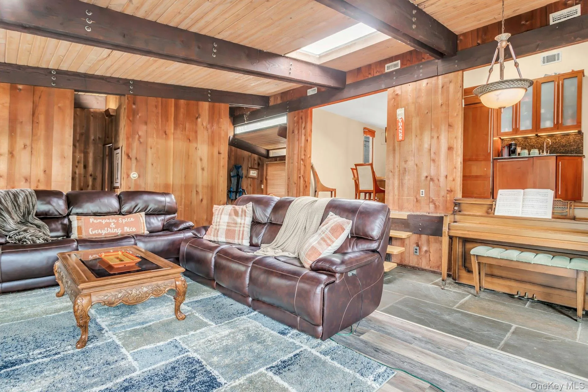 Exposed wood beams, skylight, stone flooring, wood paneling, and a built-in wet bar with upper cabinetry Exposed wood beams, skylight, stone flooring, wood paneling, and a built-in wet bar with upper cabinetry