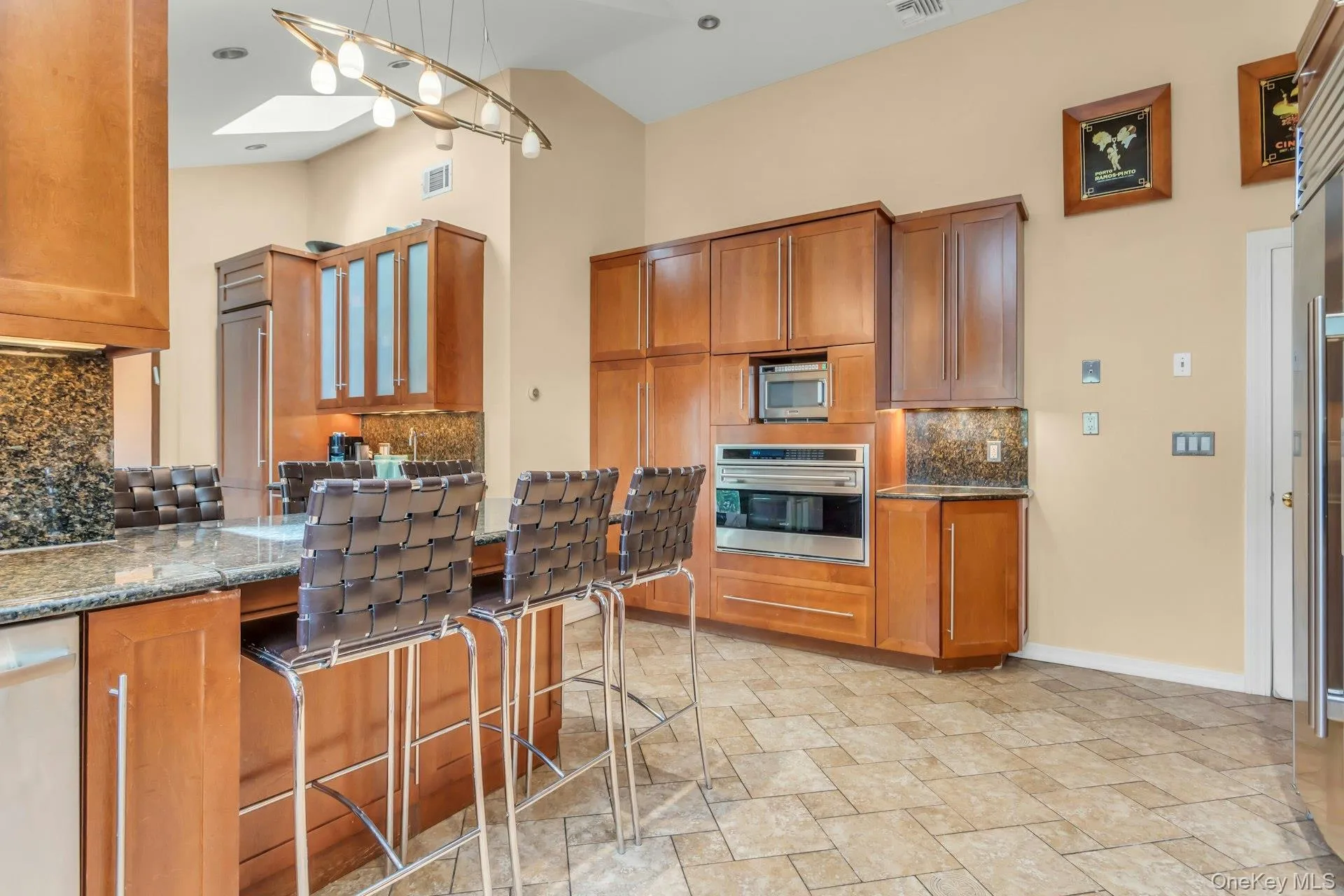 Kitchen featuring a large island with stone countertop, wood cabinetry, built-in stainless steel appliances, and tiled flooring Kitchen featuring a large island with stone countertop, wood cabinetry, built-in stainless steel appliances, and tiled flooring