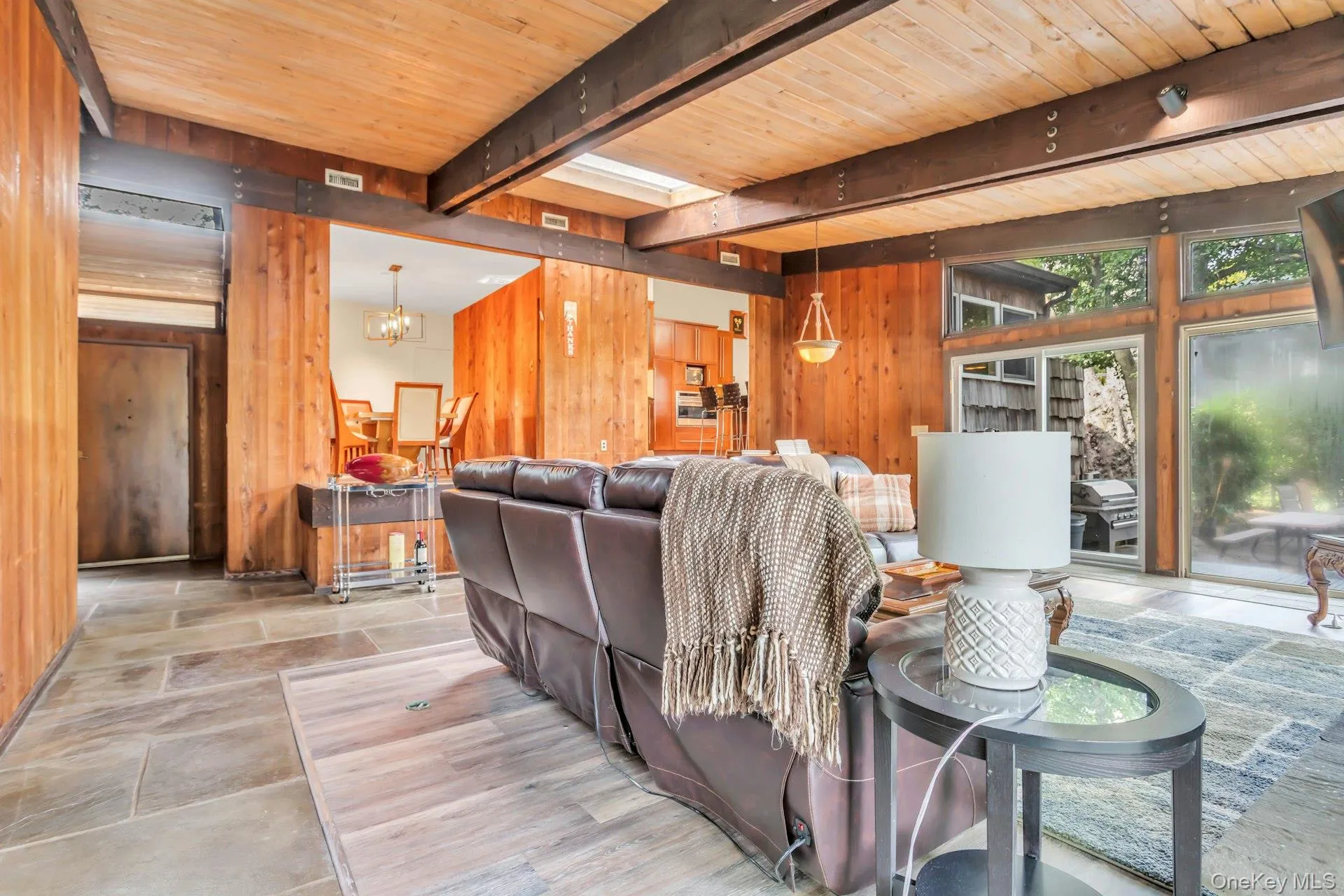 Stone tile flooring, wood panel walls, exposed beam ceiling, and a large glass sliding door Stone tile flooring, wood panel walls, exposed beam ceiling, and a large glass sliding door