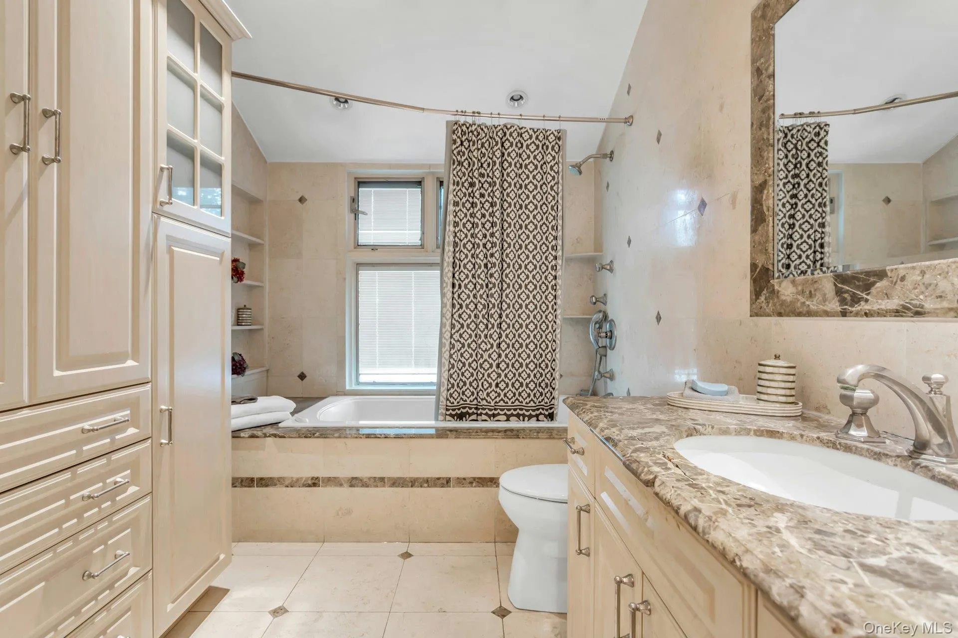 Built-in cabinetry with glass-front uppers, an undermount sink with a single-handle faucet, a built-in tub, and tiled walls with decorative accents Built-in cabinetry with glass-front uppers, an undermount sink with a single-handle faucet, a built-in tub, and tiled walls with decorative accents