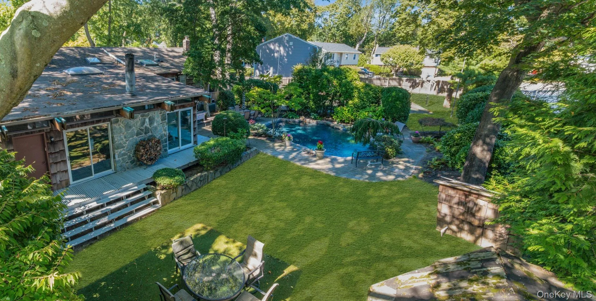 Expansive outdoor area featuring a swimming pool, stone patio, large lawn, mature landscaping, and a multi-level deck with sliding glass doors Expansive outdoor area featuring a swimming pool, stone patio, large lawn, mature landscaping, and a multi-level deck with sliding glass doors
