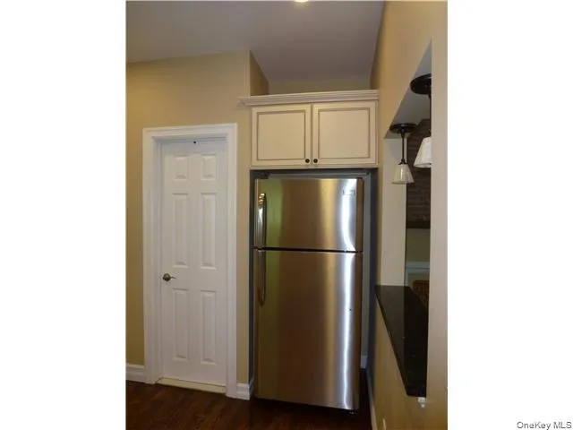 Stainless steel refrigerator, white shaker-style cabinetry, black countertop, dark wood-finish flooring, and a paneled white door Stainless steel refrigerator, white shaker-style cabinetry, black countertop, dark wood-finish flooring, and a paneled white door