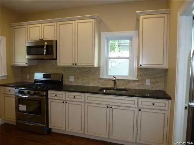 White cabinetry, dark countertops, a tile backsplash, stainless steel appliances, and a stainless steel sink White cabinetry, dark countertops, a tile backsplash, stainless steel appliances, and a stainless steel sink
