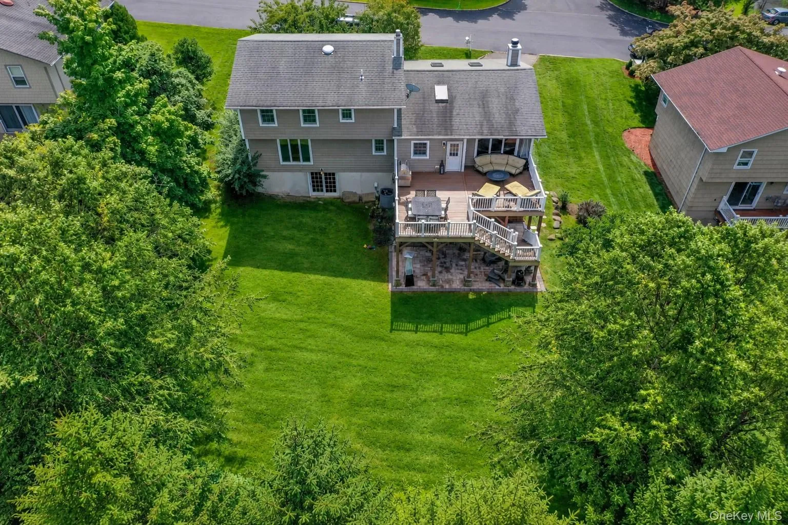 A bird's-eye view showcases the expansive backyard and oversized deck, with a stone patio and hot tub below - offering abundant space for outdoor dining, lounging, play and entertaining. A bird's-eye view showcases the expansive backyard and oversized deck, with a stone patio and hot tub below - offering abundant space for outdoor dining, lounging, play and entertaining.