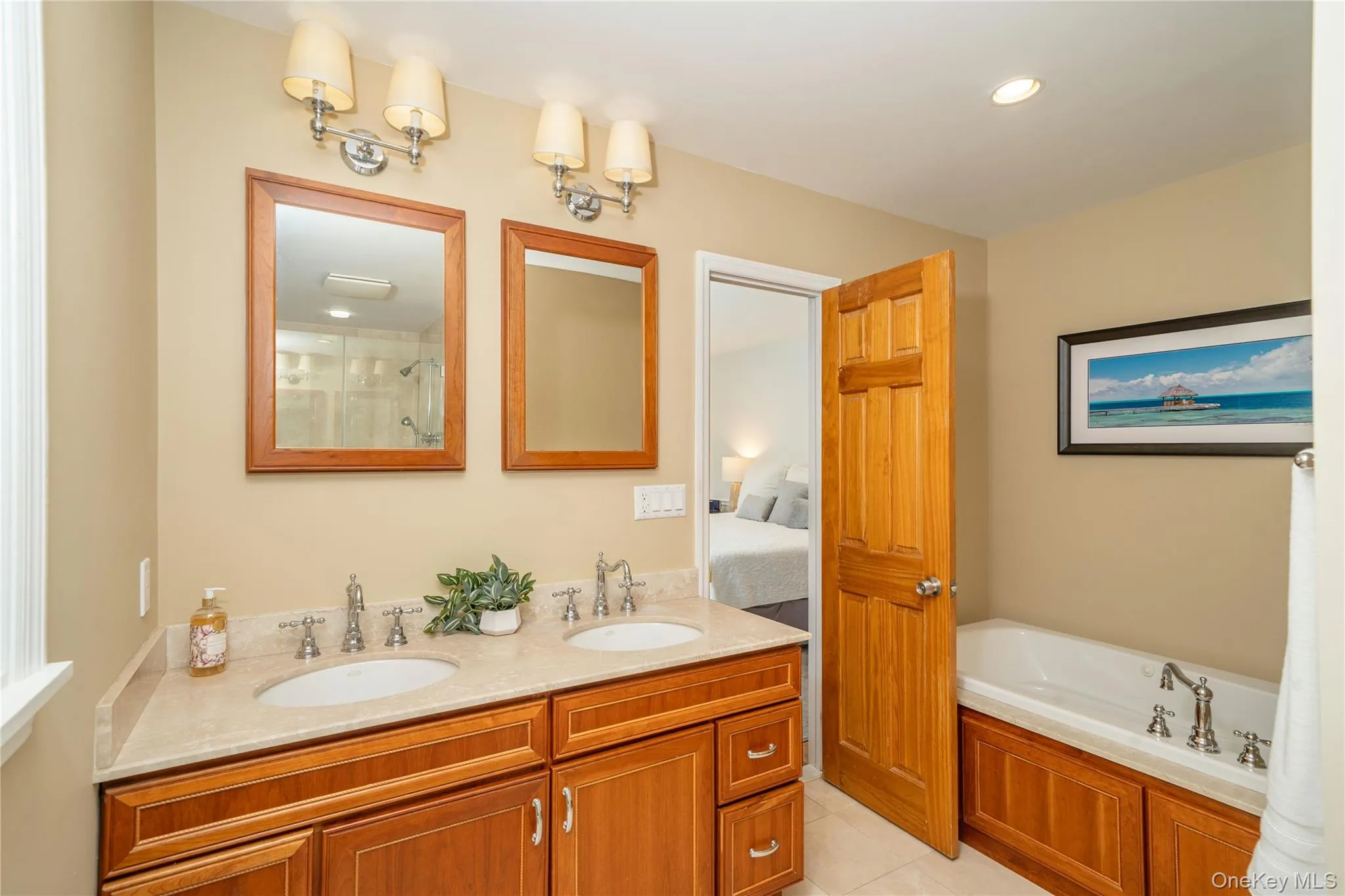 The en-suite primary bath features a double-sink vanity and jetted soaking tub, along with a separate glass-enclosed shower just beyond the frame. The en-suite primary bath features a double-sink vanity and jetted soaking tub, along with a separate glass-enclosed shower just beyond the frame.