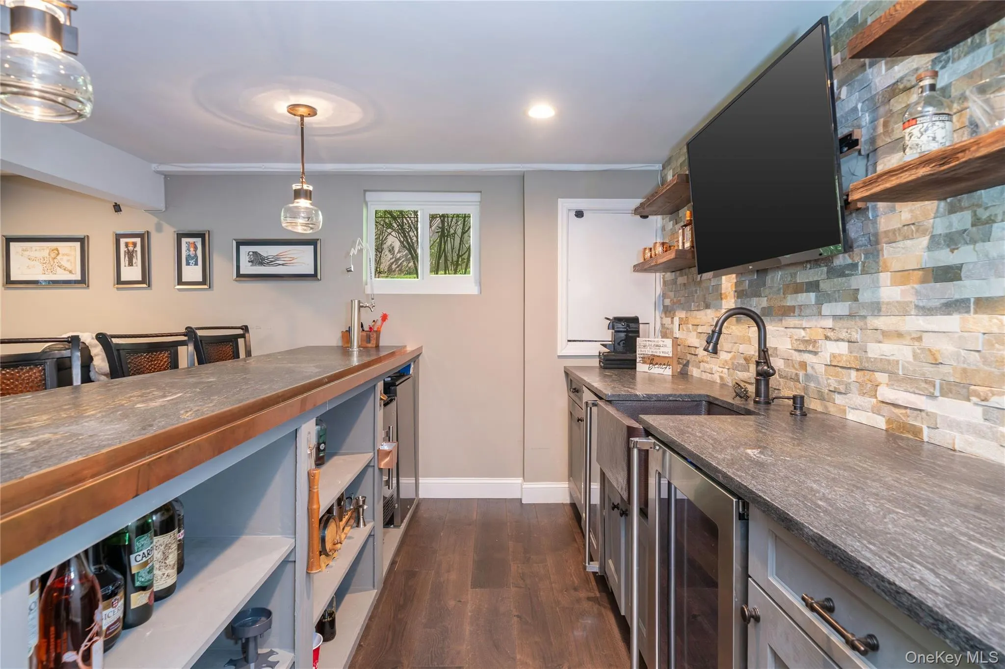 An impressive full wet bar is a standout entertaining feature, with leathered granite countertops, a stone-tiled backsplash, floating shelves, sink, refrigerator, kegerator and abundant under-counter storage. Counter seating accommodates at least four barstools, while a second TV completes this well-equipped gathering space. An impressive full wet bar is a standout entertaining feature, with leathered granite countertops, a stone-tiled backsplash, floating shelves, sink, refrigerator, kegerator and abundant under-counter storage. Counter seating accommodates at least four barstools, while a second TV completes this well-equipped gathering space.