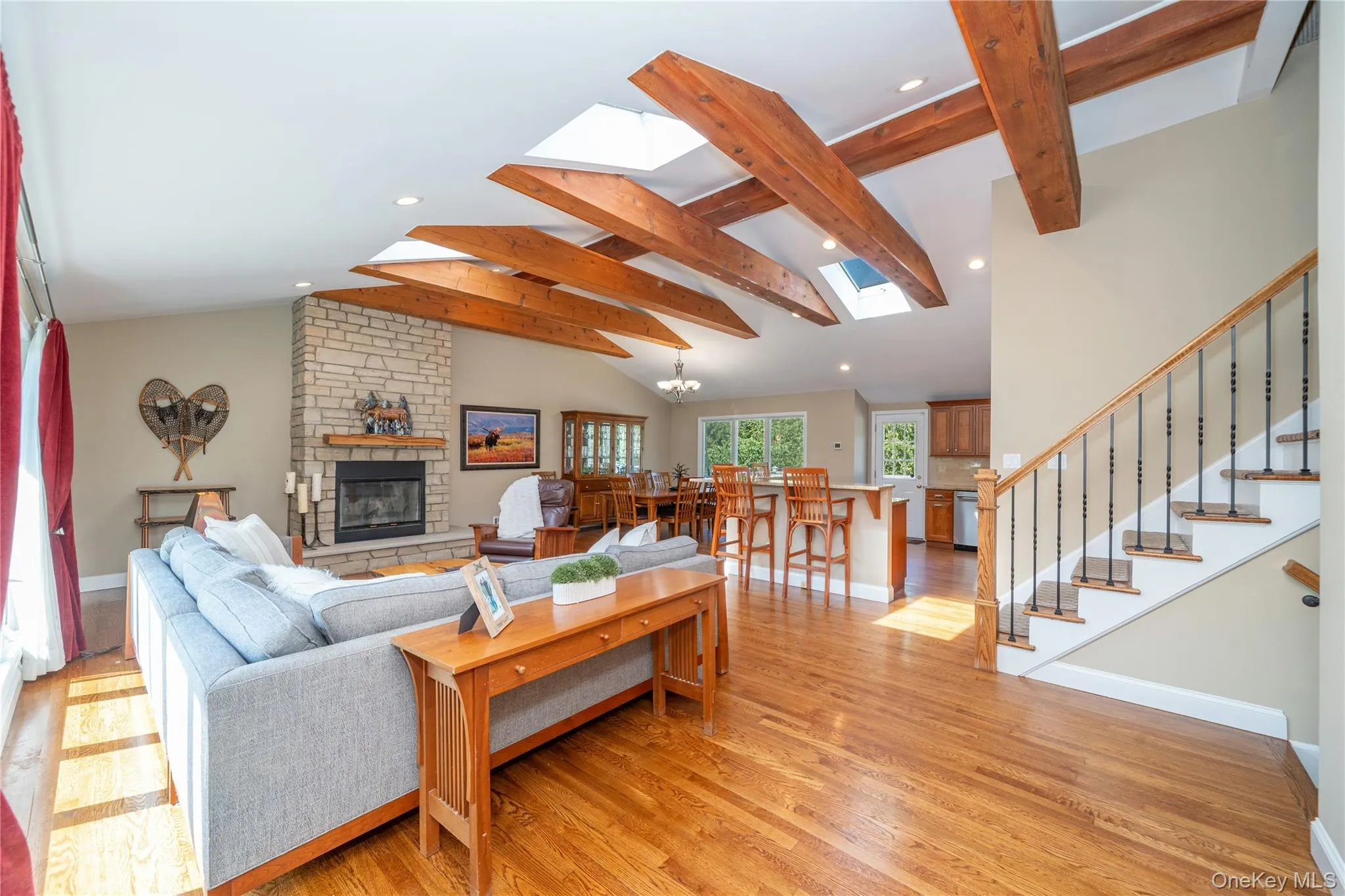 The dramatic main living area features soaring vaulted ceilings with exposed wood beams, beautiful hardwood floors and a striking stone fireplace, creating a warm and inviting space for both everyday living and entertaining. The dramatic main living area features soaring vaulted ceilings with exposed wood beams, beautiful hardwood floors and a striking stone fireplace, creating a warm and inviting space for both everyday living and entertaining.