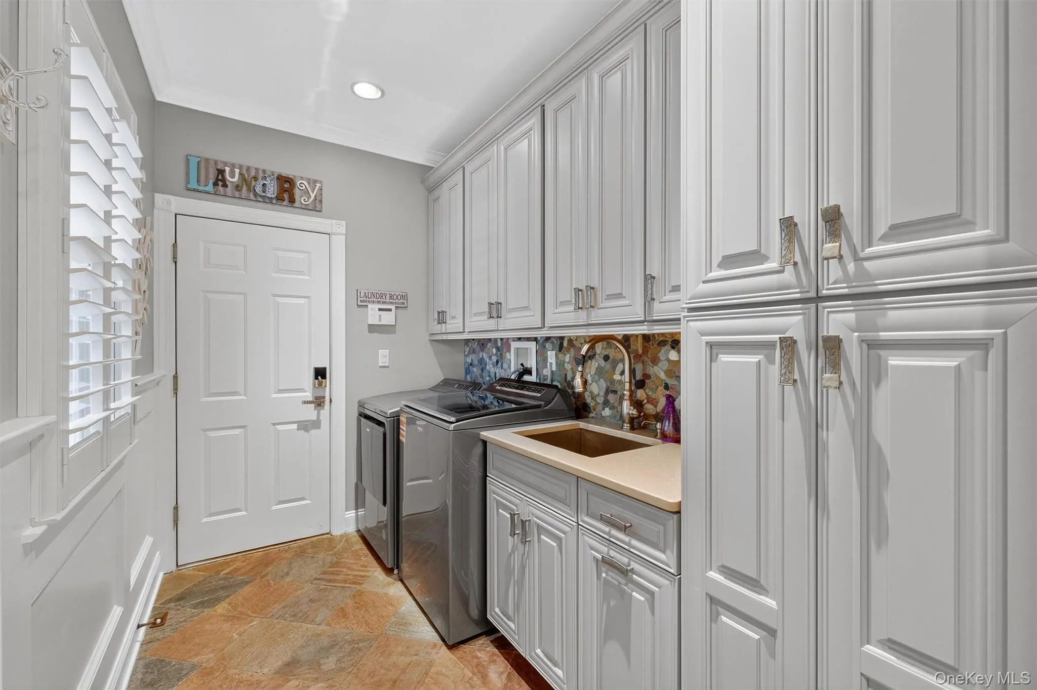 This well-designed laundry room, conveniently located just off the kitchen with direct access to the garage, combines function with style. Outfitted with custom cabinetry and ??countertops & finished with a Mosaic backsplash. It offers floor to ceiling cabinetry for plenty of storage and workspace to keep everything organized. A front-loading washer and gas dryer make laundry tasks efficient, while the thoughtful layout ensures this everyday space feels both practical and polished. Now "you don't have to air your dirty laundry" Literally!! This well-designed laundry room, conveniently located just off the kitchen with direct access to the garage, combines function with style. Outfitted with custom cabinetry and ??countertops & finished with a Mosaic backsplash. It offers floor to ceiling cabinetry for plenty of storage and workspace to keep everything organized. A front-loading washer and gas dryer make laundry tasks efficient, while the thoughtful layout ensures this everyday space feels both practical and polished. Now "you don't have to air your dirty laundry" Literally!!