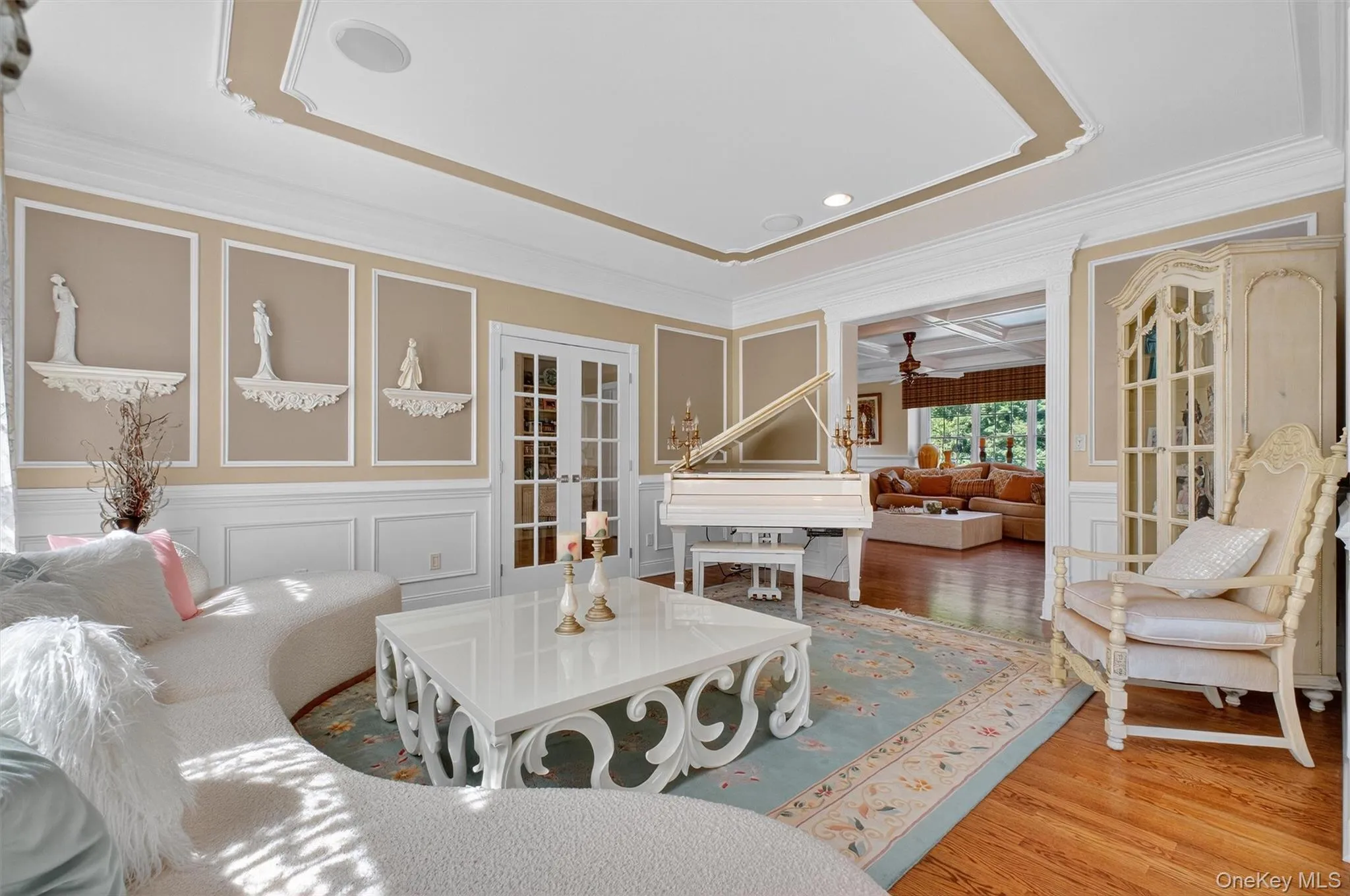 Step into this elegant formal living room, where timeless design meets sophisticated charm. The room features a beautifully crafted tray ceiling with gold-toned accents that add depth and architectural interest. Ornate wall panel molding provides a classic backdrop, complemented by neutral taupe and white tones that enhance the sense of space and light.Perfect for entertaining or relaxing in style, this living room exudes luxury and grace with every detail. Step into this elegant formal living room, where timeless design meets sophisticated charm. The room features a beautifully crafted tray ceiling with gold-toned accents that add depth and architectural interest. Ornate wall panel molding provides a classic backdrop, complemented by neutral taupe and white tones that enhance the sense of space and light.Perfect for entertaining or relaxing in style, this living room exudes luxury and grace with every detail.