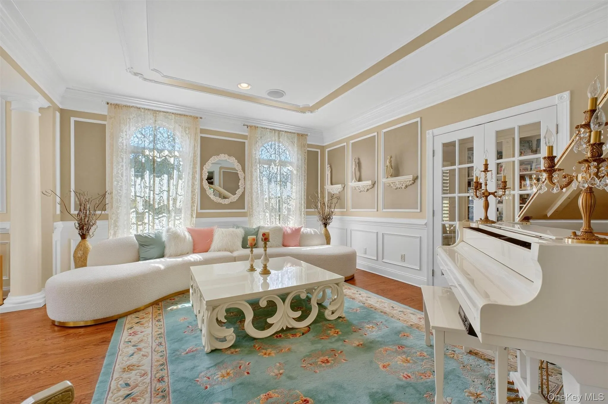 This stunning formal living room radiates elegance and charm, showcasing a sophisticated tray ceiling with gold trim detailing that adds height and visual interest. The space is filled with natural light streaming through floor-to-ceiling windows adorned with delicate drapery, creating a warm and inviting atmosphereElegant French doors lead to adjacent living spaces, maintaining an open flow while preserving the room’s intimate feel.Classic wainscoting and paneled walls enhance the traditional design, while decorative niches with sculptural accents lend a refined, gallery-like touchElegant French doors lead to adjacent living spaces, maintaining an open flow while preserving the room’s intimate feel. This stunning formal living room radiates elegance and charm, showcasing a sophisticated tray ceiling with gold trim detailing that adds height and visual interest. The space is filled with natural light streaming through floor-to-ceiling windows adorned with delicate drapery, creating a warm and inviting atmosphereElegant French doors lead to adjacent living spaces, maintaining an open flow while preserving the room’s intimate feel.Classic wainscoting and paneled walls enhance the traditional design, while decorative niches with sculptural accents lend a refined, gallery-like touchElegant French doors lead to adjacent living spaces, maintaining an open flow while preserving the room’s intimate feel.