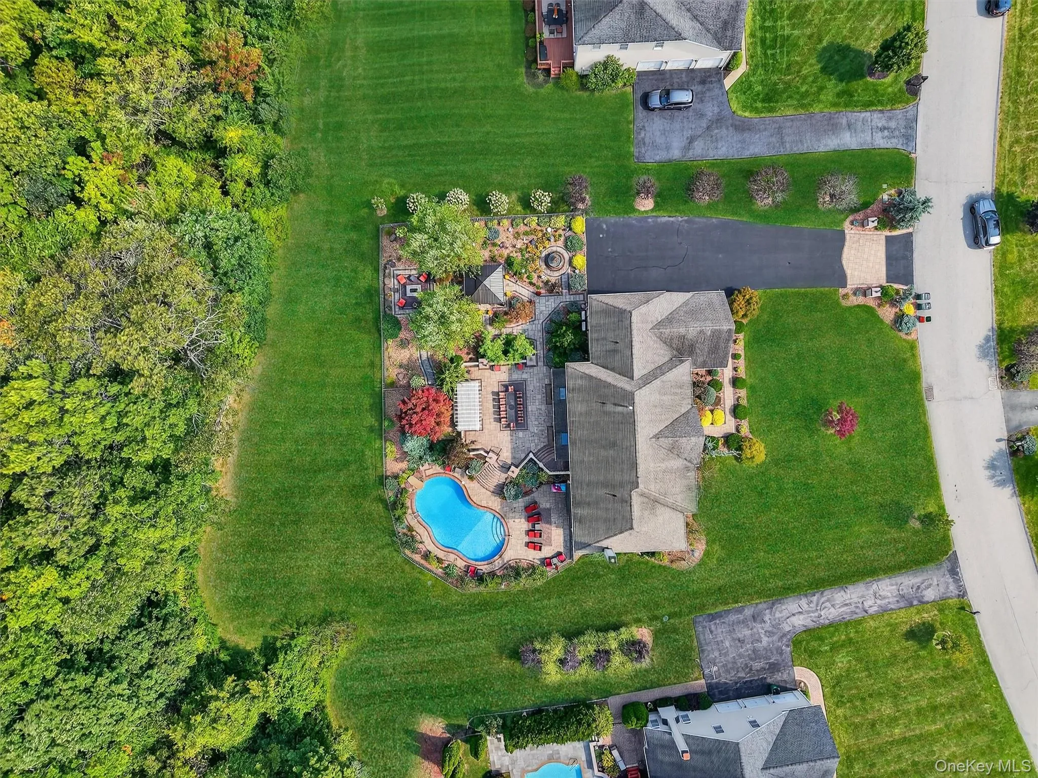 The second image reveals the full scope of this nearly 1-acre corner estate, where the home is gracefully positioned amidst manicured lawns and a long, private driveway that enhances its refined, estate-like presence. The backyard emerges as the crown jewel—lush, expansive, and bordered by a serene stretch of mature woods, offering unmatched privacy and a picturesque natural backdrop. From this aerial vantage, the thoughtful layout becomes evident: resort-style pool, expansive patios, intimate garden retreats, and seamless transitions from curated landscaping to open green space. The property’s orientation provides a generous buffer from neighboring homes, creating a rare balance of seclusion and grandeur, all within a prestigious and tranquil community setting. The second image reveals the full scope of this nearly 1-acre corner estate, where the home is gracefully positioned amidst manicured lawns and a long, private driveway that enhances its refined, estate-like presence. The backyard emerges as the crown jewel—lush, expansive, and bordered by a serene stretch of mature woods, offering unmatched privacy and a picturesque natural backdrop. From this aerial vantage, the thoughtful layout becomes evident: resort-style pool, expansive patios, intimate garden retreats, and seamless transitions from curated landscaping to open green space. The property’s orientation provides a generous buffer from neighboring homes, creating a rare balance of seclusion and grandeur, all within a prestigious and tranquil community setting.