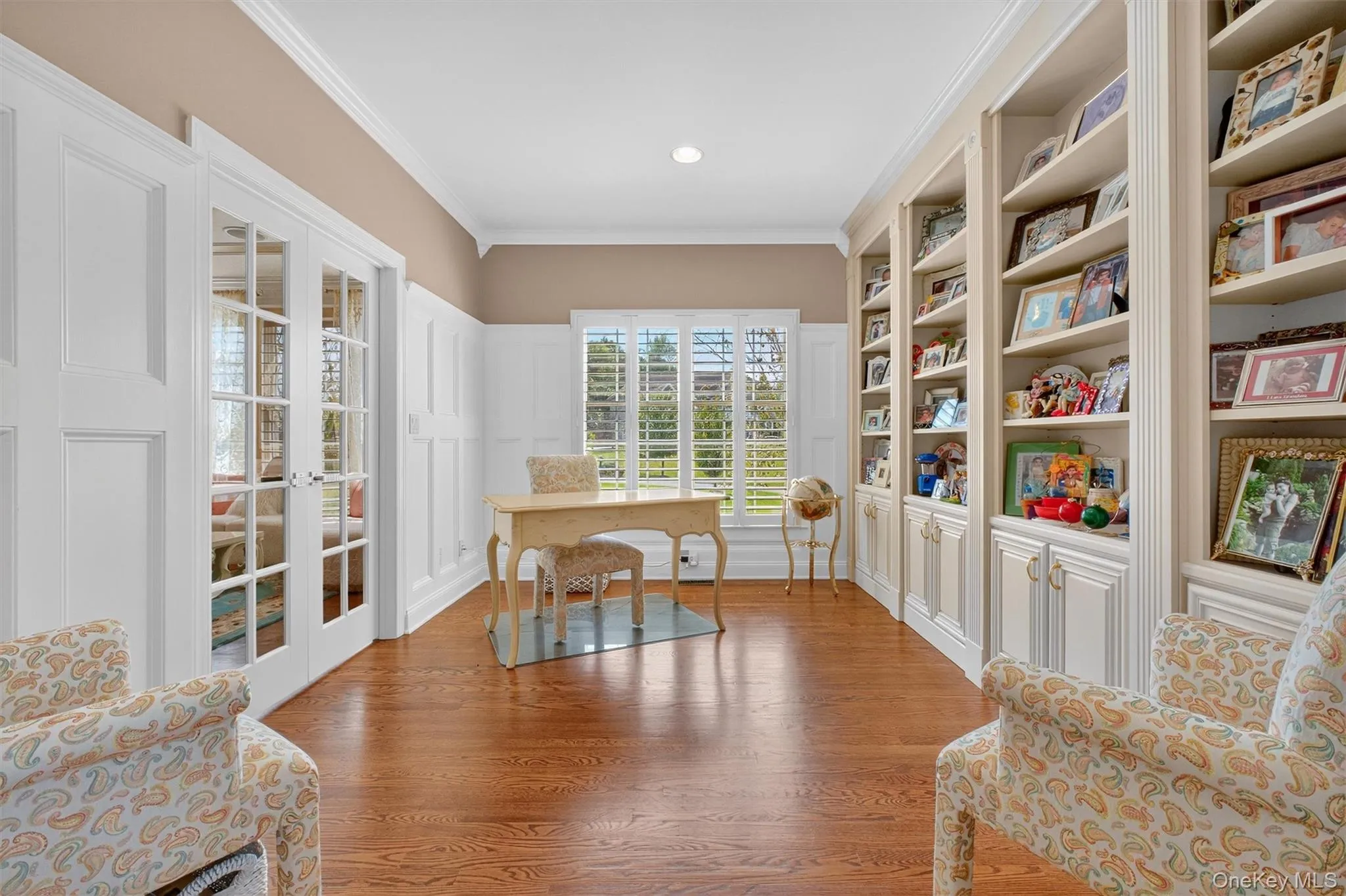 This bright and inviting home office is flooded with natural light, thanks to a large window overlooking the frontyard and two sets of double French doors that gracefully connect it to both the living and family rooms. These doors not only allow for seamless flow between spaces, but also offer privacy when needed—making the room perfect for focused work or quiet reflectionCustom built-in bookshelves span the wall, currently styled as a heartfelt display of cherished family memories, friends, and loved ones—a beautiful reminder of what truly makes a house a home. The warm hardwood floors, soft neutral tones, and cozy sitting area create a space that feels both elegant and personal.Whether used as a study, library, or memory-filled retreat, this room offers a perfect balance of functionality and emotional warmth. This bright and inviting home office is flooded with natural light, thanks to a large window overlooking the frontyard and two sets of double French doors that gracefully connect it to both the living and family rooms. These doors not only allow for seamless flow between spaces, but also offer privacy when needed—making the room perfect for focused work or quiet reflectionCustom built-in bookshelves span the wall, currently styled as a heartfelt display of cherished family memories, friends, and loved ones—a beautiful reminder of what truly makes a house a home. The warm hardwood floors, soft neutral tones, and cozy sitting area create a space that feels both elegant and personal.Whether used as a study, library, or memory-filled retreat, this room offers a perfect balance of functionality and emotional warmth.