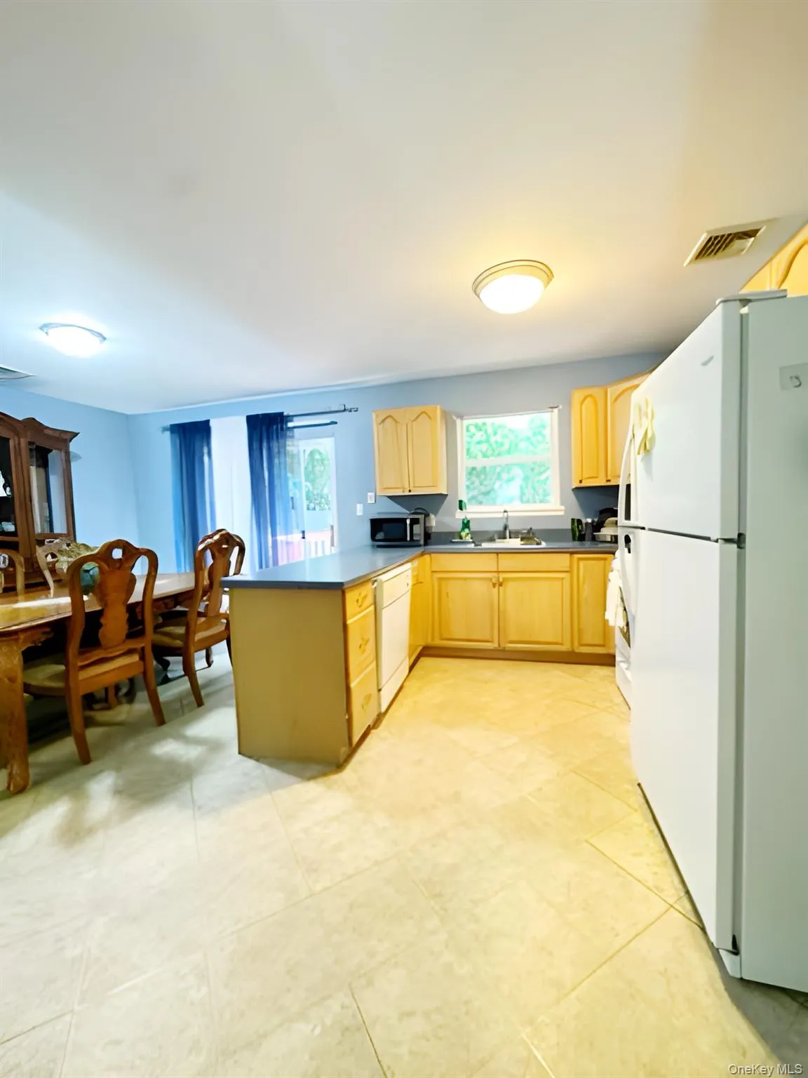 Kitchen with white appliances, light brown cabinetry, a peninsula, and healthy amount of natural light Kitchen with white appliances, light brown cabinetry, a peninsula, and healthy amount of natural light