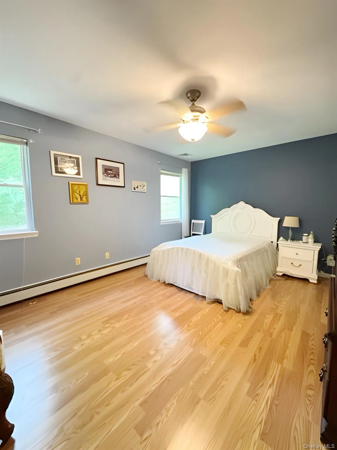 Bedroom featuring light wood finished floors, ceiling fan, and a baseboard heating unit Bedroom featuring light wood finished floors, ceiling fan, and a baseboard heating unit