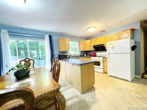 Kitchen with white appliances, light brown cabinets, a peninsula, ventilation hood, and light tile patterned flooring Kitchen with white appliances, light brown cabinets, a peninsula, ventilation hood, and light tile patterned flooring
