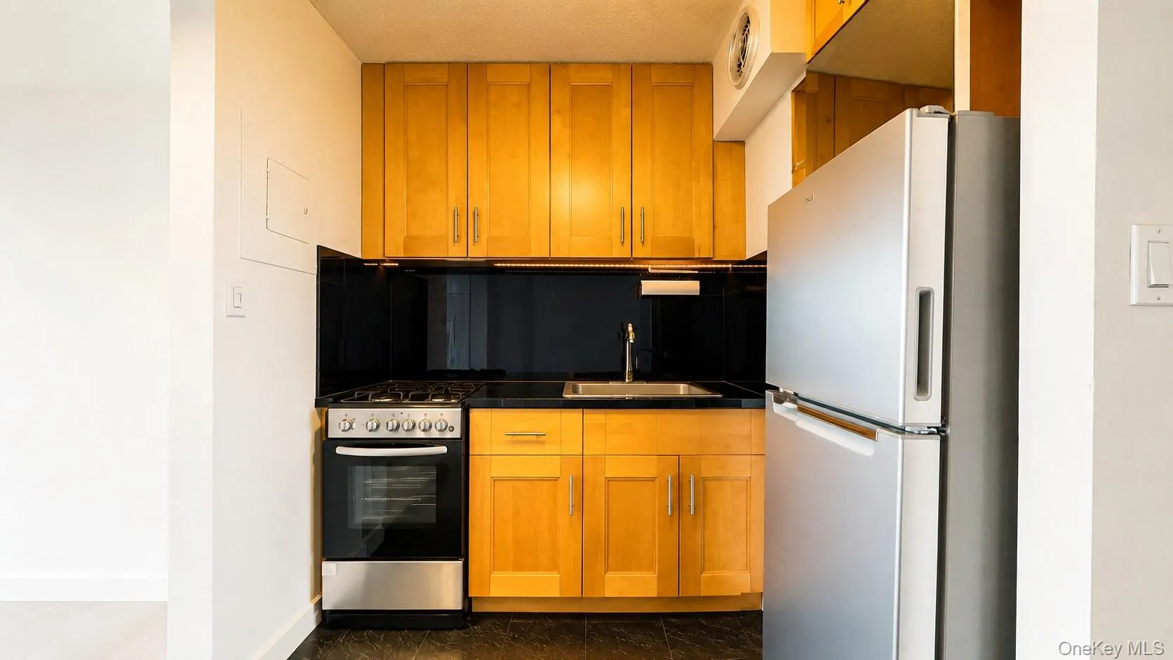 Compact kitchen featuring light wood cabinetry, stainless steel appliances, sleek Black Granite countertops, and a stainless steel sink with a gooseneck faucet Compact kitchen featuring light wood cabinetry, stainless steel appliances, sleek Black Granite countertops, and a stainless steel sink with a gooseneck faucet