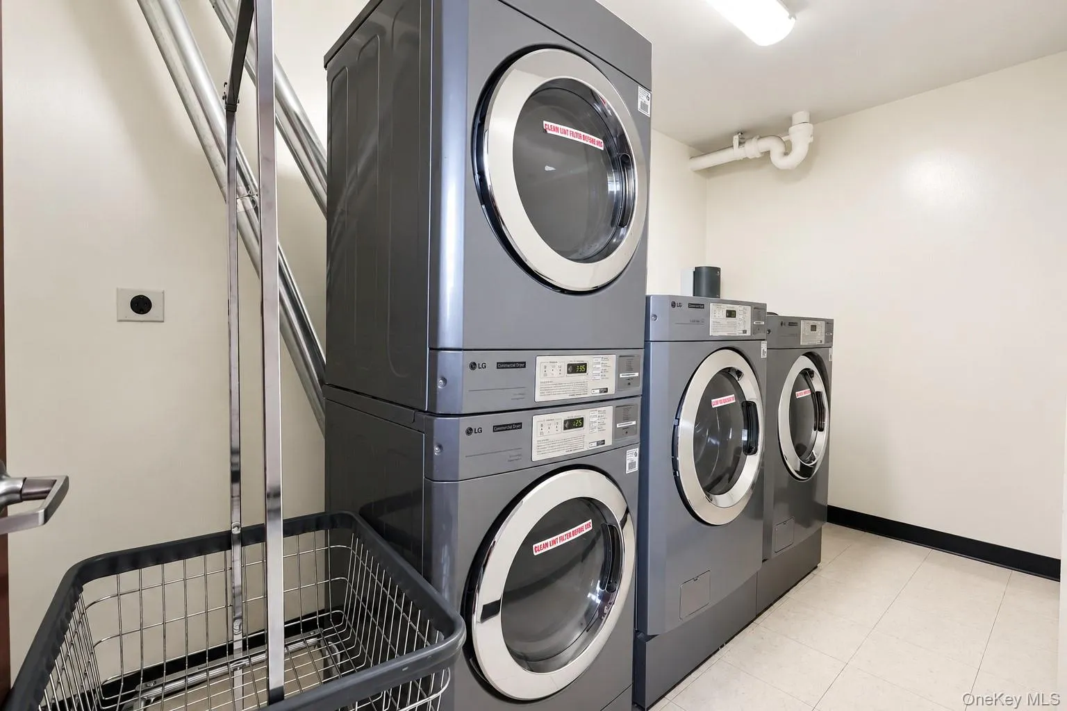 Dedicated laundry area featuring multiple stacked and side-by-side front-loading washers and dryers, overhead fluorescent lighting, and light-colored floor tiles Dedicated laundry area featuring multiple stacked and side-by-side front-loading washers and dryers, overhead fluorescent lighting, and light-colored floor tiles