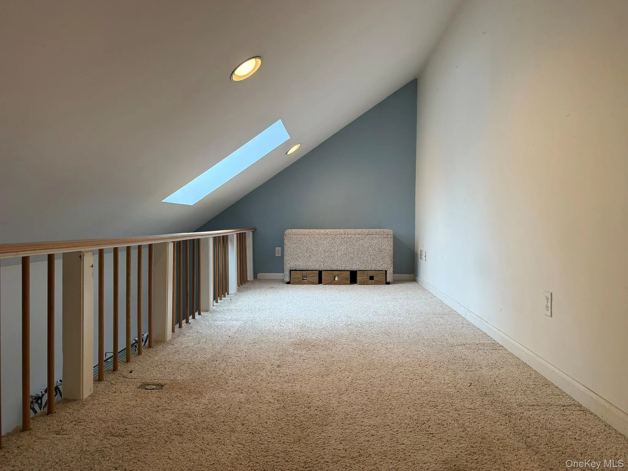 Upstairs loft with recessed lighting, skylight, carpeted flooring, and a wooden railing with vertical spindles Upstairs loft with recessed lighting, skylight, carpeted flooring, and a wooden railing with vertical spindles