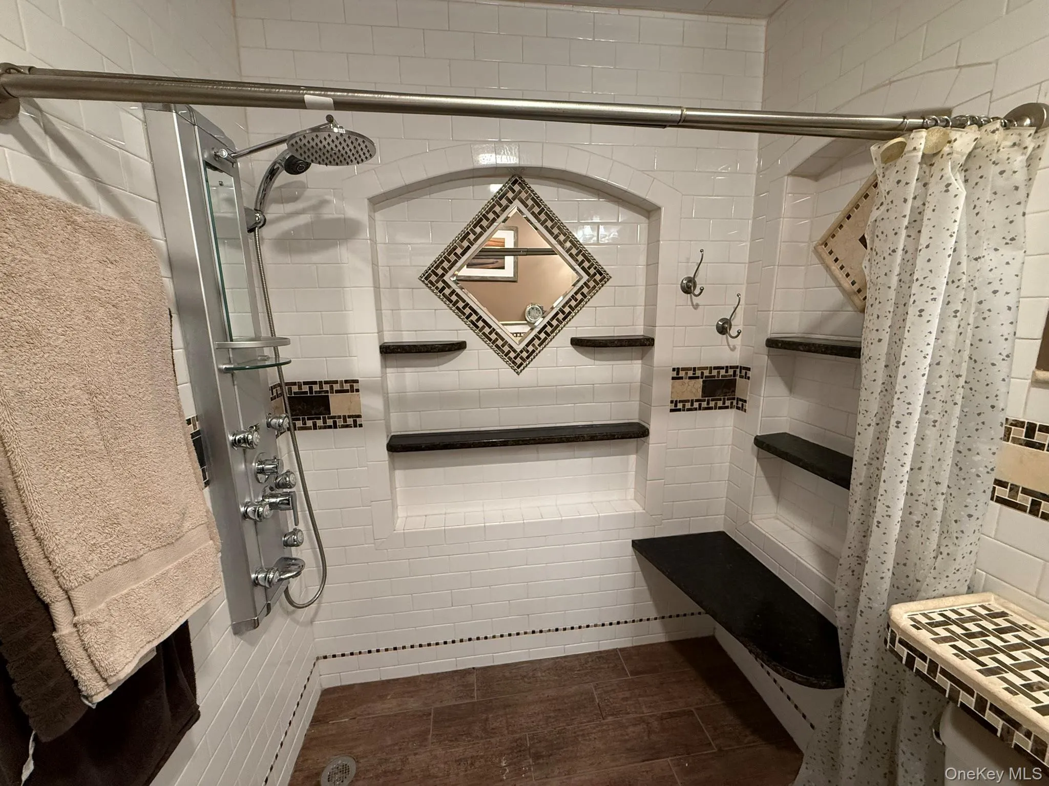 Shower stall featuring white subway tile, a multi-function shower panel, built-in shelving, a built-in bench Shower stall featuring white subway tile, a multi-function shower panel, built-in shelving, a built-in bench