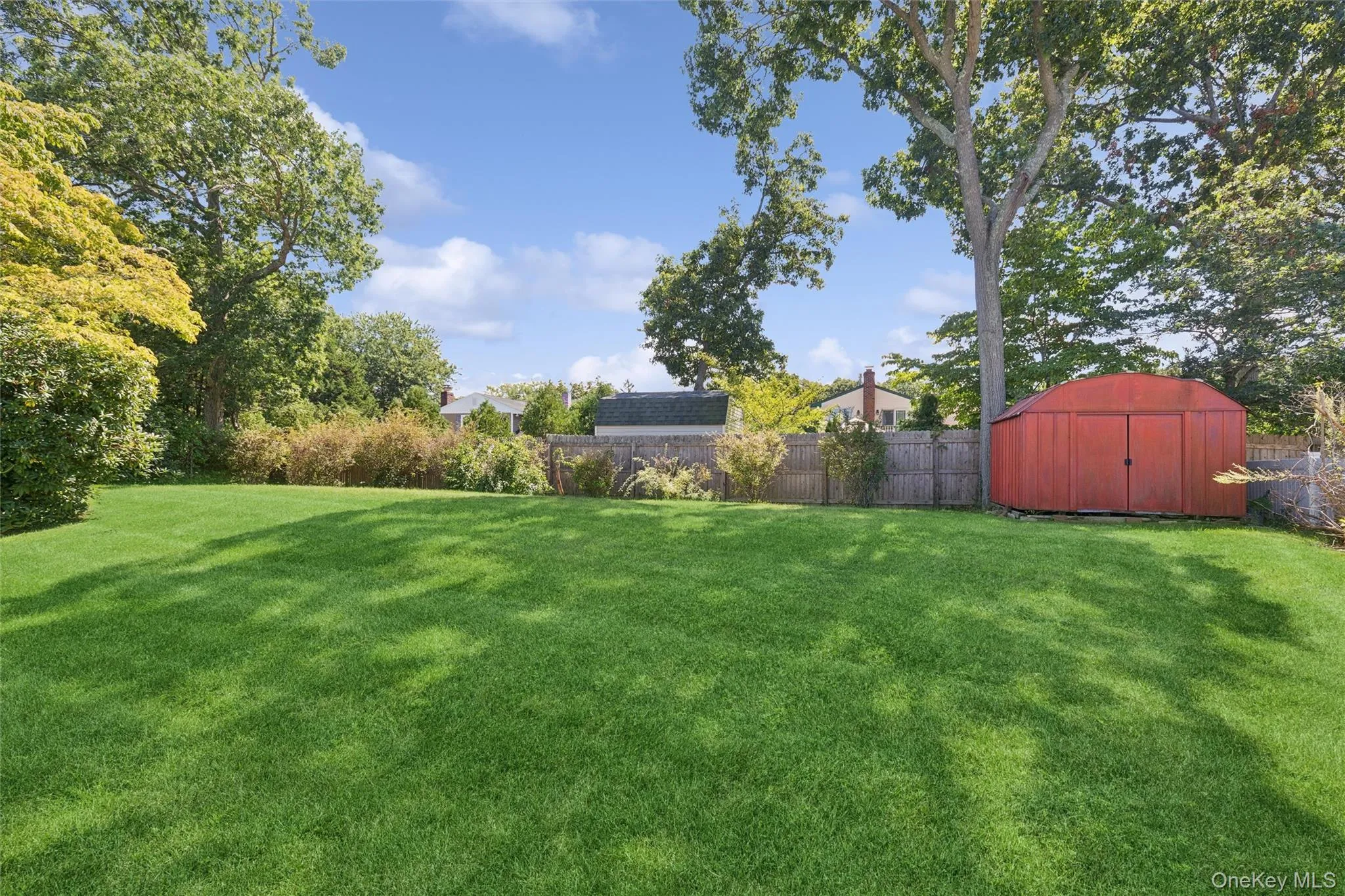 Expansive backyard featuring a manicured lawn, mature trees, wood fence, and a red storage shed Expansive backyard featuring a manicured lawn, mature trees, wood fence, and a red storage shed