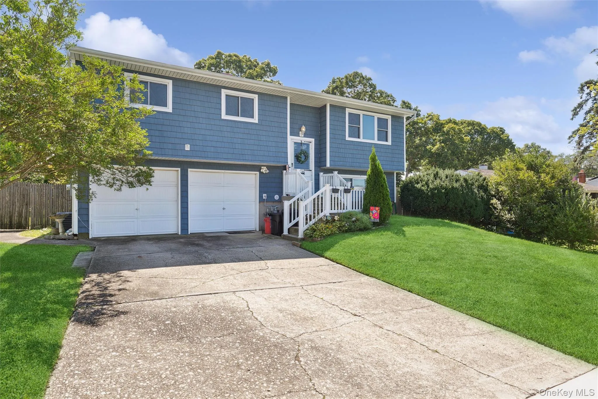 Split-level residence featuring blue siding, a two-car garage, white railings, and a sloped lawn Split-level residence featuring blue siding, a two-car garage, white railings, and a sloped lawn