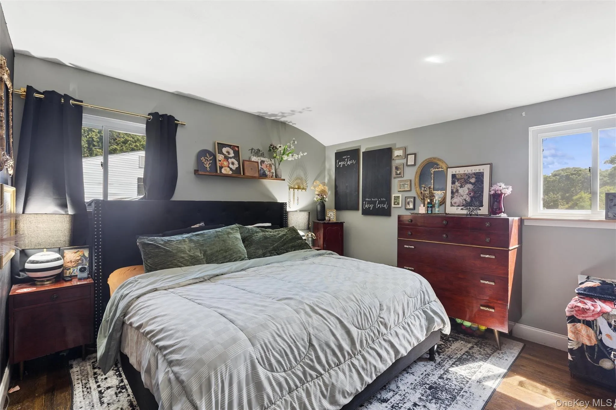 Recessed ceiling lighting, light gray wall paint, wood-finish flooring, white window frames, and a dark upholstered headboard Recessed ceiling lighting, light gray wall paint, wood-finish flooring, white window frames, and a dark upholstered headboard