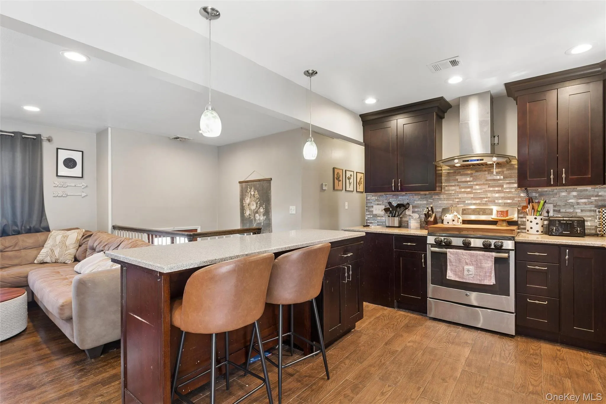 Kitchen featuring dark wood cabinetry, stainless steel appliances, a tiled backsplash, and a breakfast bar with pendant lighting Kitchen featuring dark wood cabinetry, stainless steel appliances, a tiled backsplash, and a breakfast bar with pendant lighting