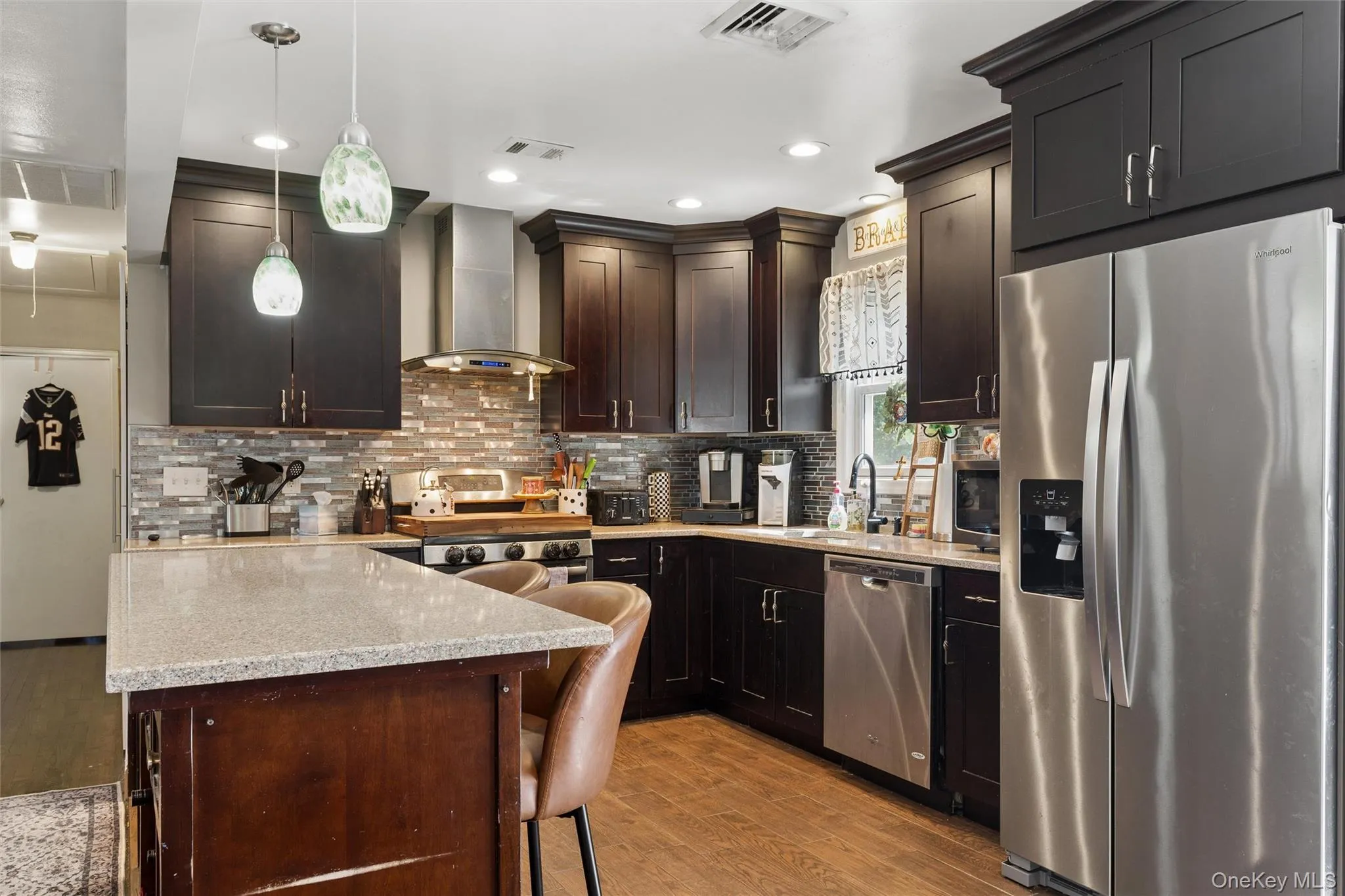 Kitchen featuring dark wood cabinetry, stainless steel appliances, a mosaic tile backsplash, a kitchen island with a light-colored countertop, and recessed lighting Kitchen featuring dark wood cabinetry, stainless steel appliances, a mosaic tile backsplash, a kitchen island with a light-colored countertop, and recessed lighting