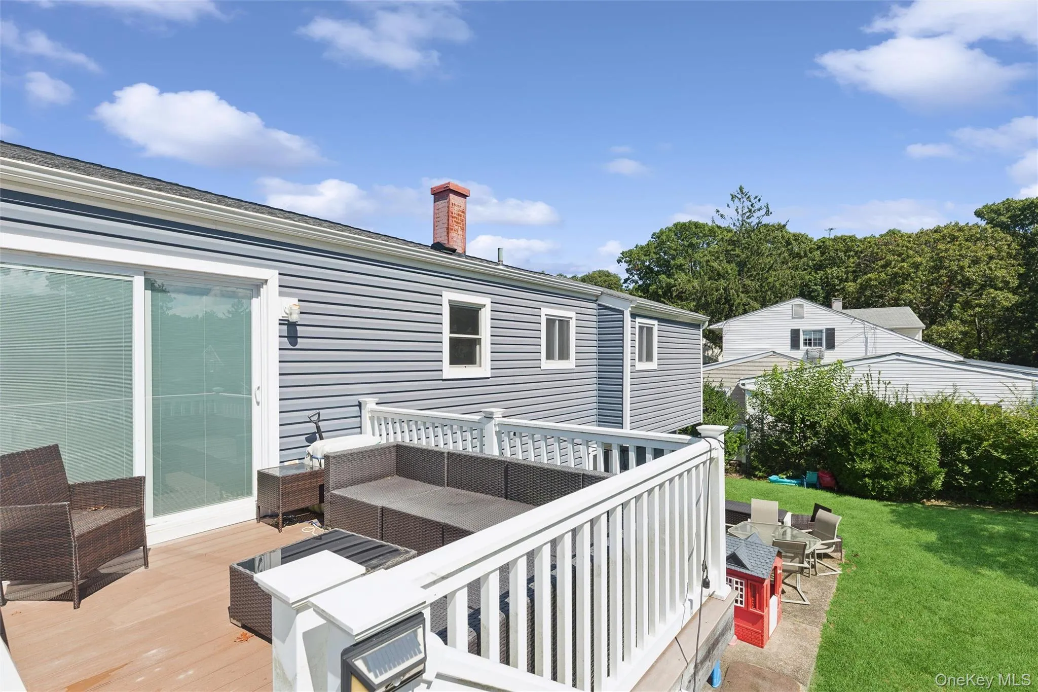Expansive wood-finish deck with white railing, sliding glass door access, and a manicured lawn Expansive wood-finish deck with white railing, sliding glass door access, and a manicured lawn
