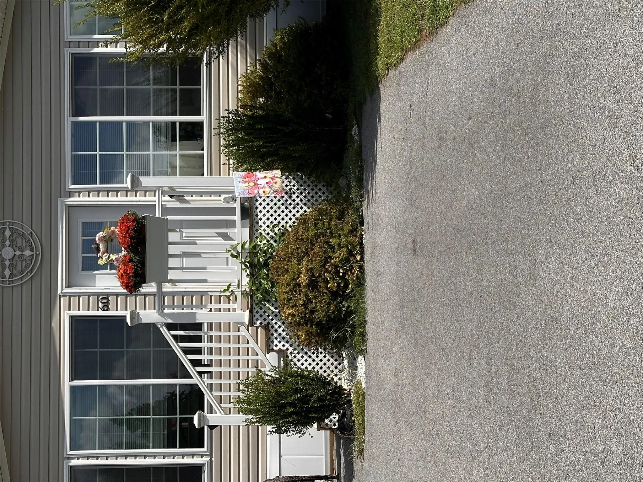 Light-toned siding exterior with a white entry door, white railings, and mature shrubbery. Light-toned siding exterior with a white entry door, white railings, and mature shrubbery.