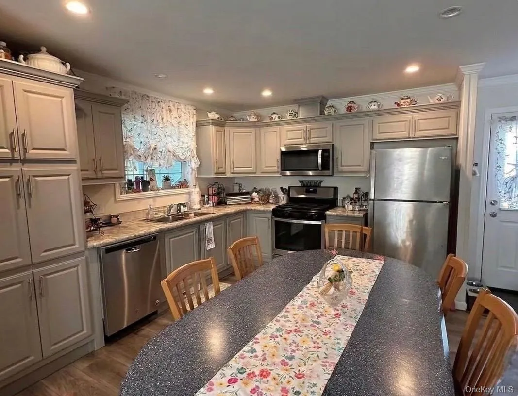 Kitchen featuring light gray cabinetry, stainless steel appliances, recessed ceiling lighting, a built-in oven, and wood-finish flooring. Kitchen featuring light gray cabinetry, stainless steel appliances, recessed ceiling lighting, a built-in oven, and wood-finish flooring.
