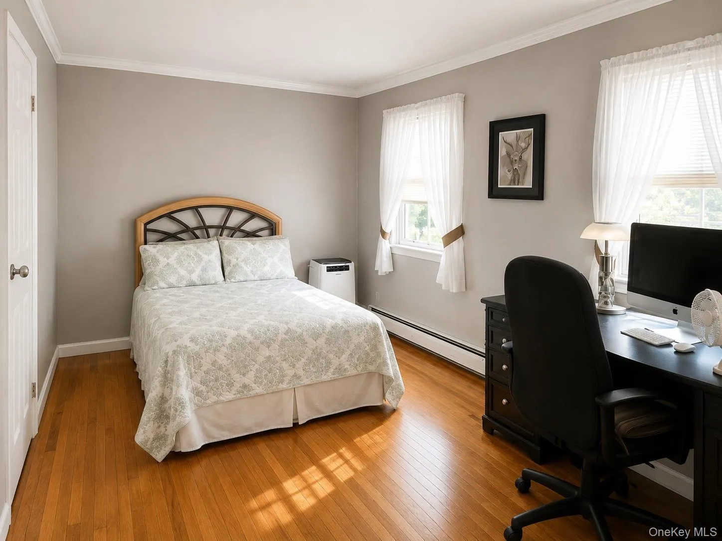 Bright, light-filled bedroom featuring hardwood flooring, a wood-frame bed with decorative headboard, and dual windows with natural light Bright, light-filled bedroom featuring hardwood flooring, a wood-frame bed with decorative headboard, and dual windows with natural light