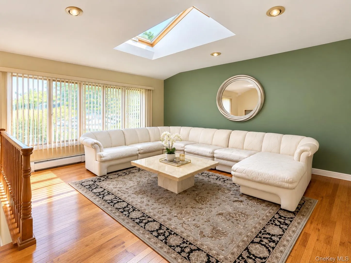Hardwood flooring, recessed lighting, and a skylight illuminate this living area with a large window and a green accent wall Hardwood flooring, recessed lighting, and a skylight illuminate this living area with a large window and a green accent wall