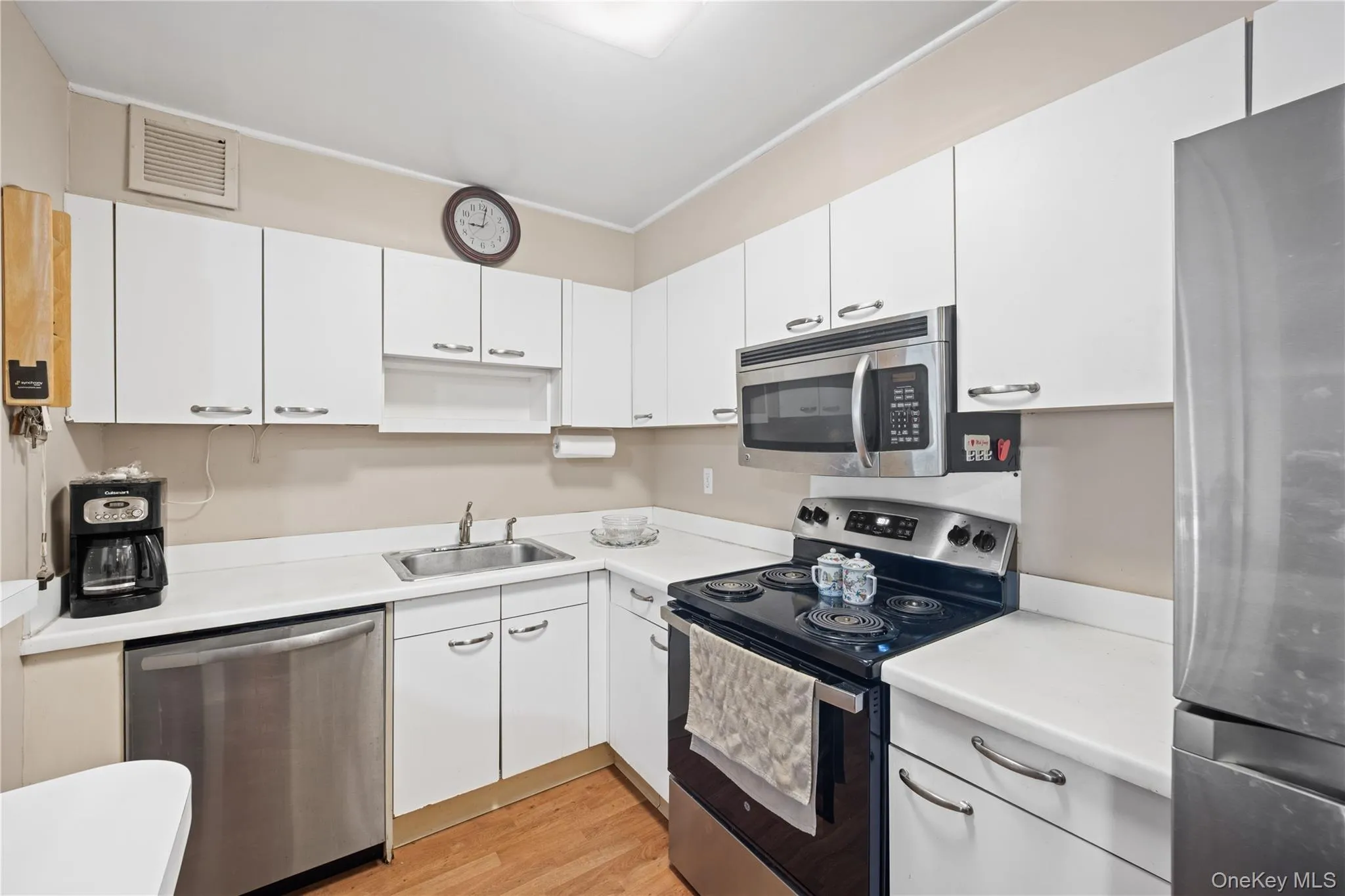 Kitchen featuring wood-finish flooring, white cabinetry with silver-tone hardware, stainless steel appliances, and a built-in microwave Kitchen featuring wood-finish flooring, white cabinetry with silver-tone hardware, stainless steel appliances, and a built-in microwave