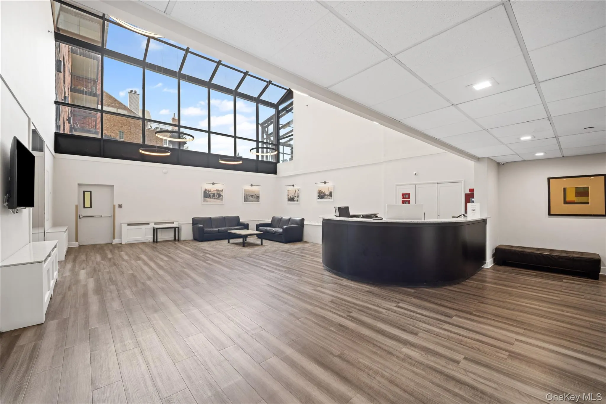 Expansive common area featuring large format window walls, wood-finish flooring, a reception desk, and recessed lighting Expansive common area featuring large format window walls, wood-finish flooring, a reception desk, and recessed lighting