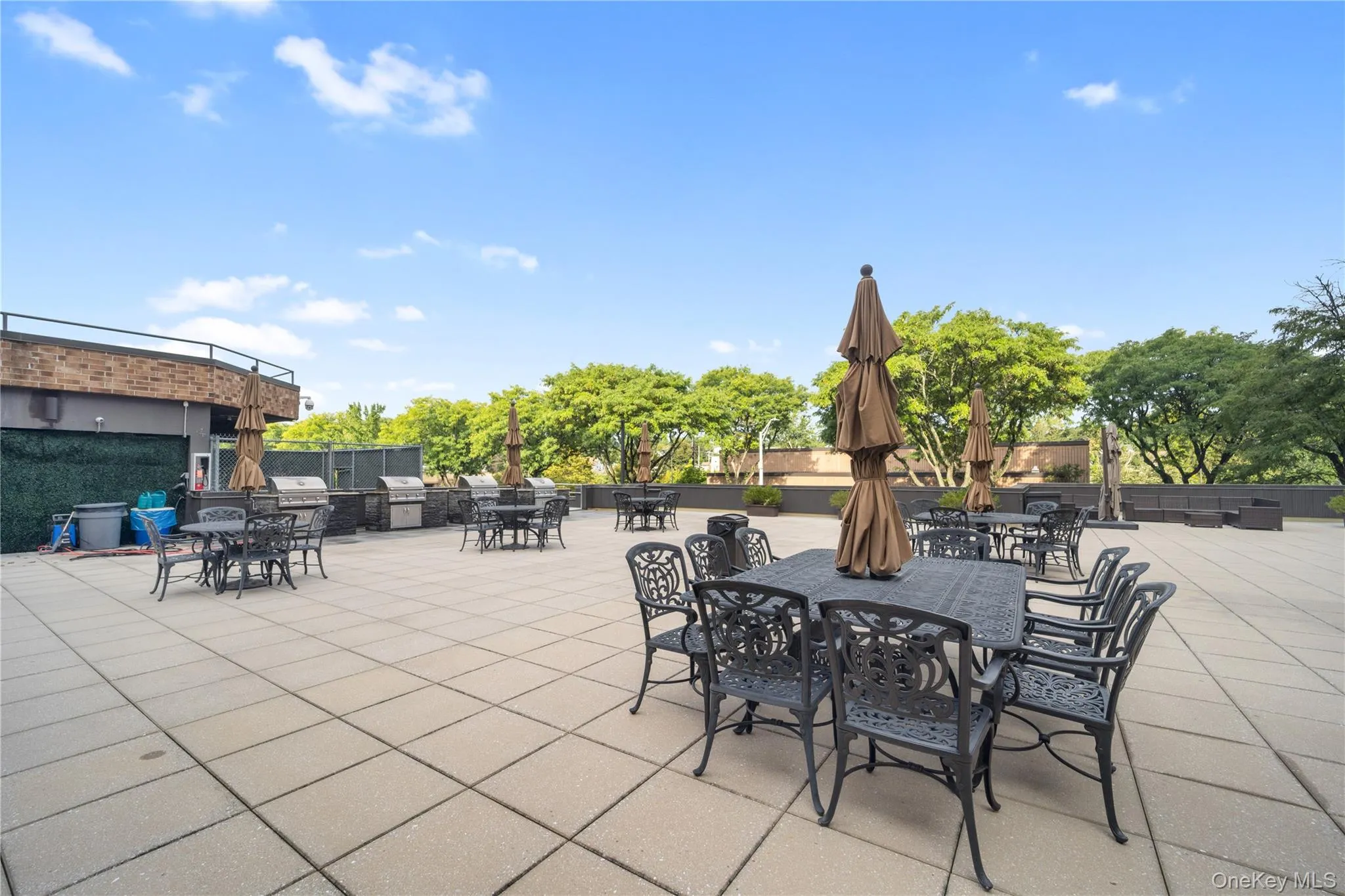 Spacious rooftop patio featuring multiple outdoor dining sets, several outdoor grills, and a large paver-stone surface Spacious rooftop patio featuring multiple outdoor dining sets, several outdoor grills, and a large paver-stone surface