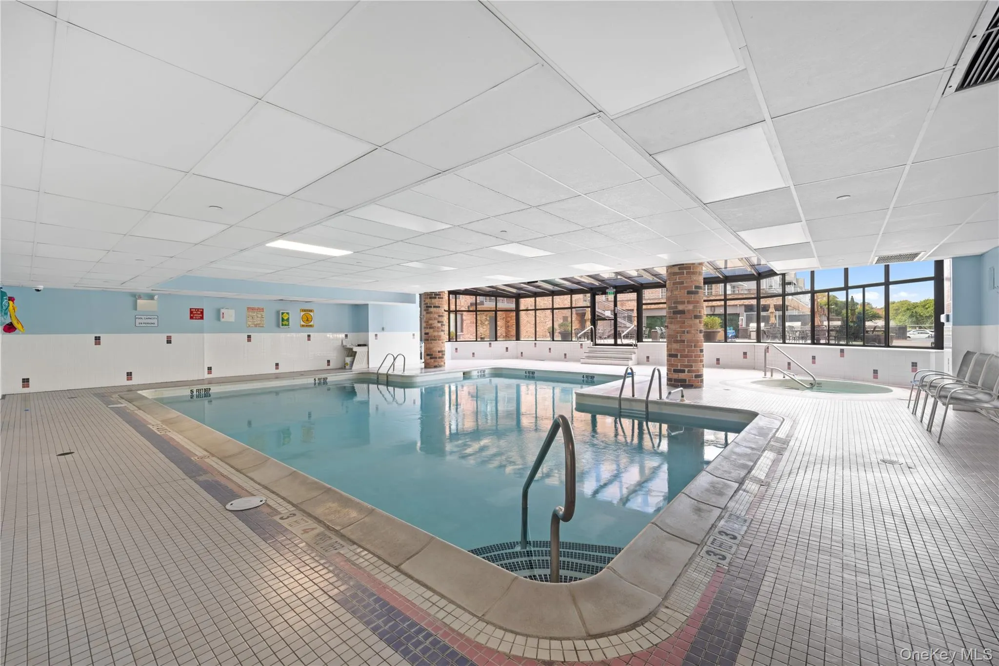 Indoor swimming pool with surrounding tiled deck, integrated hot tub, and large windows Indoor swimming pool with surrounding tiled deck, integrated hot tub, and large windows