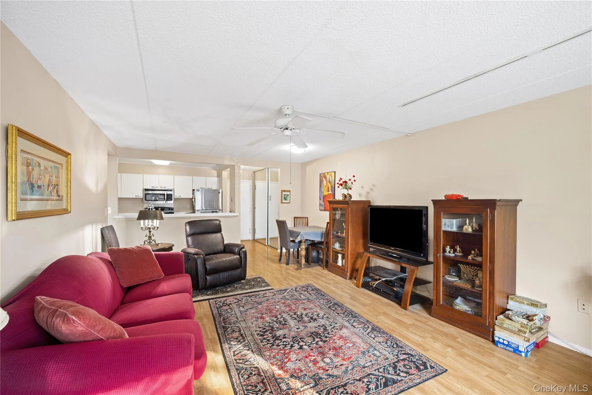 Wood-finish flooring throughout the living space, a ceiling fan with integrated lighting, and a breakfast bar separating the kitchen Wood-finish flooring throughout the living space, a ceiling fan with integrated lighting, and a breakfast bar separating the kitchen