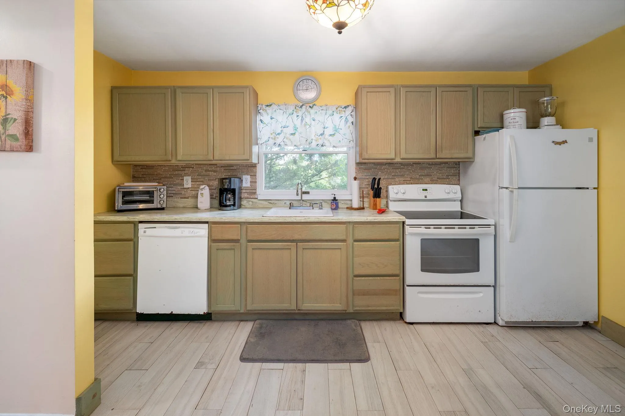 Full kitchen featuring light wood-finish cabinetry, a tile backsplash, and a built-in dishwasher Full kitchen featuring light wood-finish cabinetry, a tile backsplash, and a built-in dishwasher