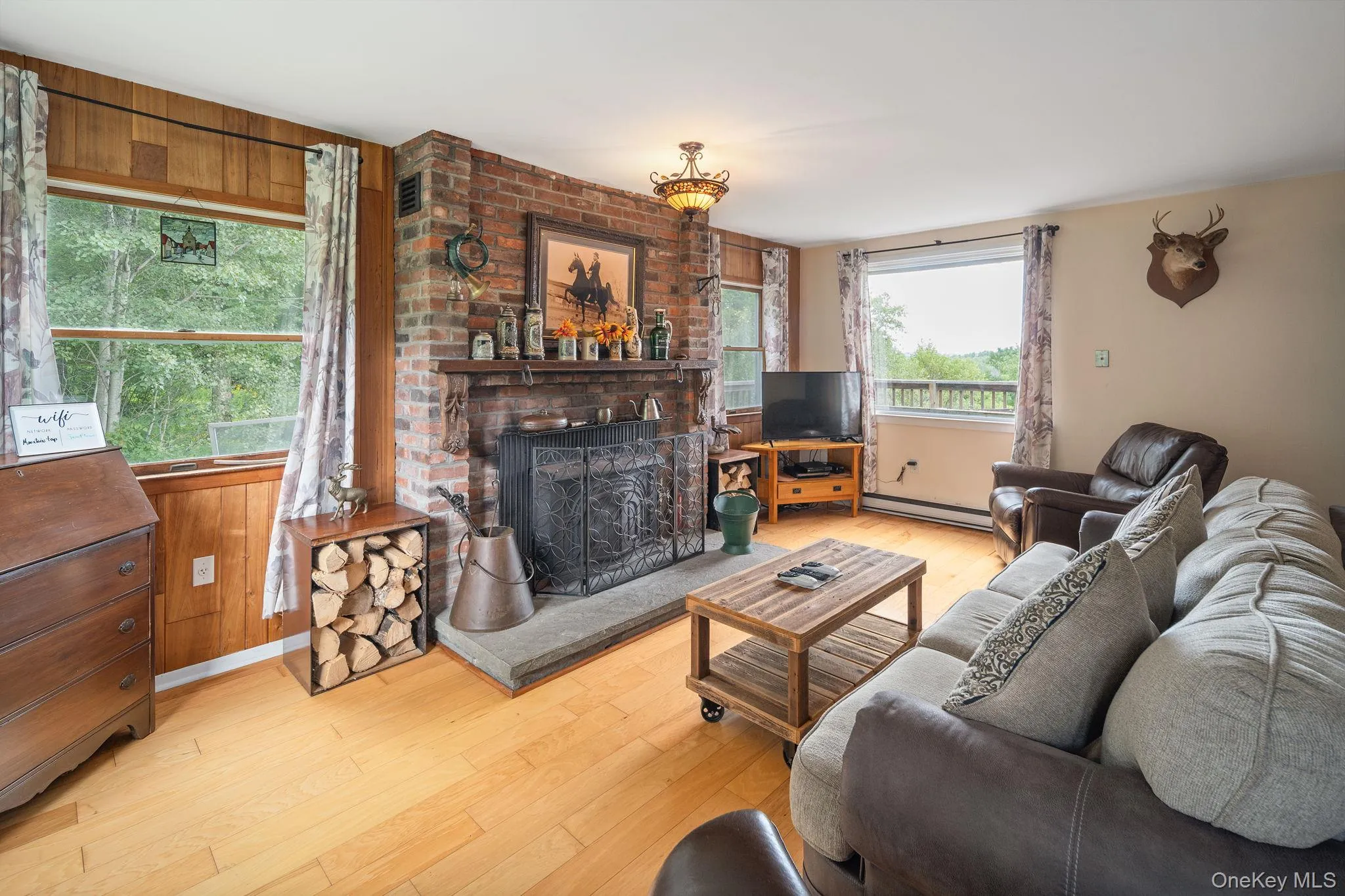 Brick fireplace with a stone hearth, wood-finish flooring, wood paneling, and an exposed beam ceiling Brick fireplace with a stone hearth, wood-finish flooring, wood paneling, and an exposed beam ceiling