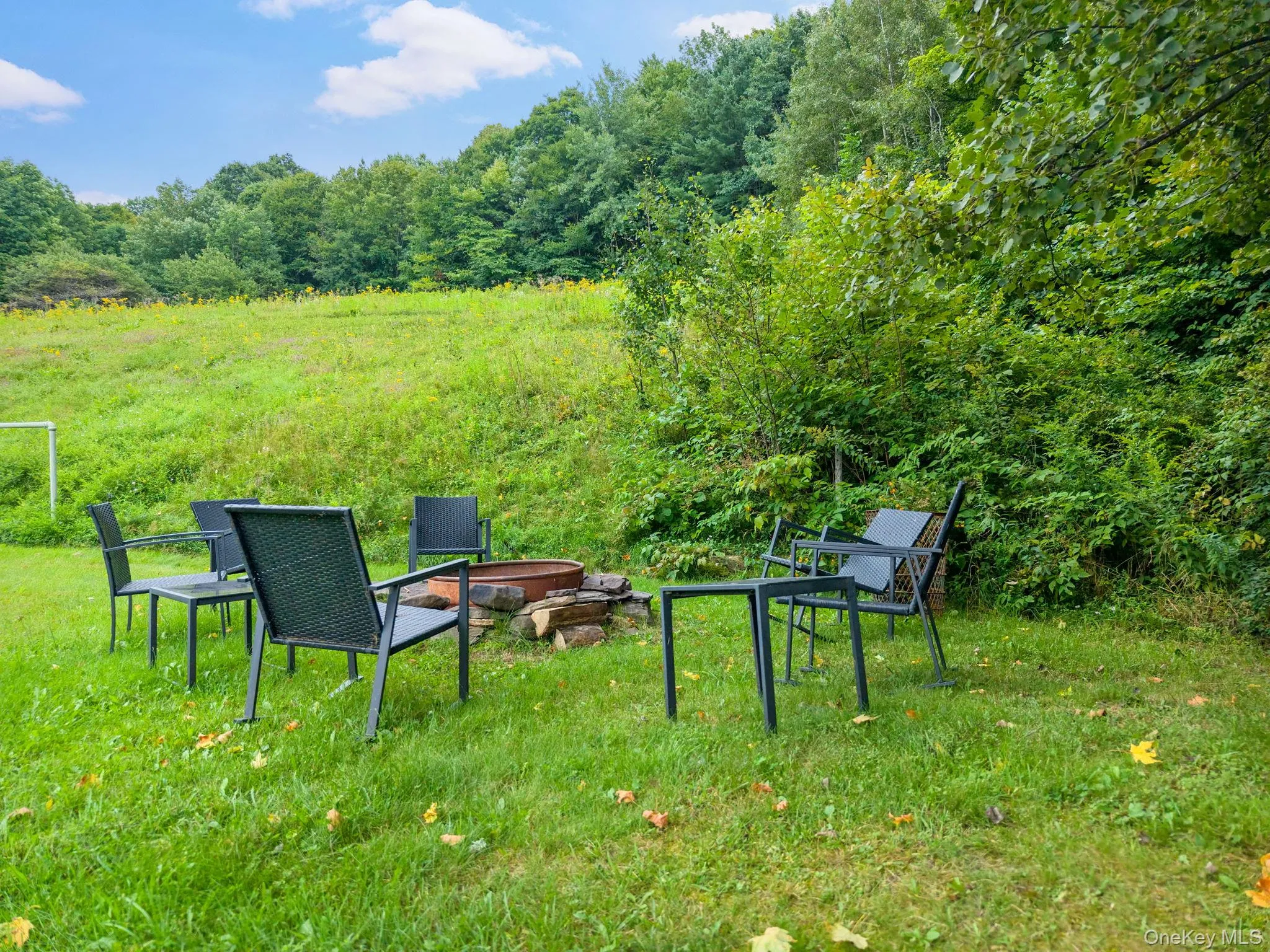 Expansive green space featuring a fire pit with stone surround and mature trees Expansive green space featuring a fire pit with stone surround and mature trees