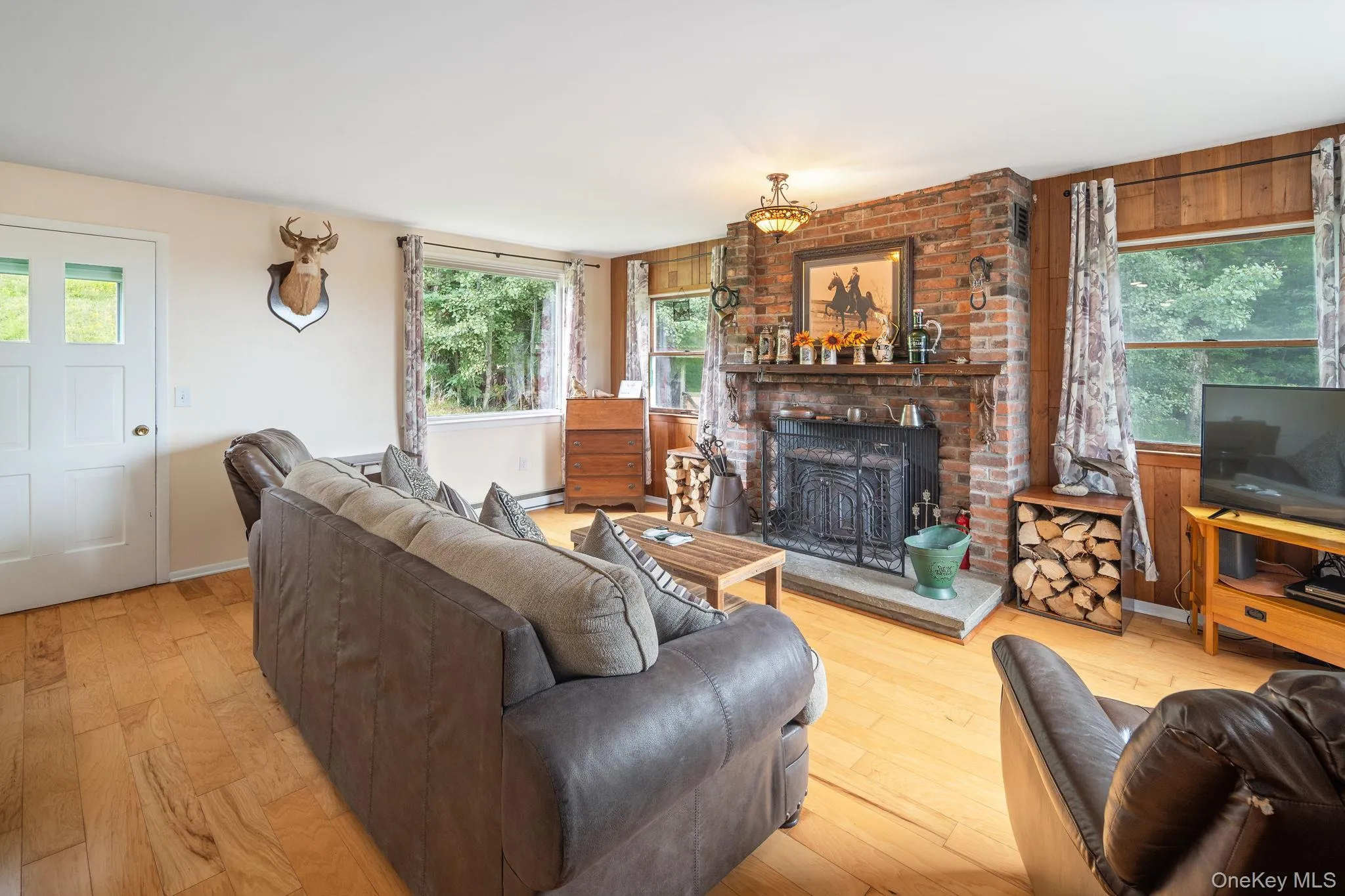 Brick-clad fireplace with a stone hearth, wood-finish flooring, and natural wood paneling Brick-clad fireplace with a stone hearth, wood-finish flooring, and natural wood paneling