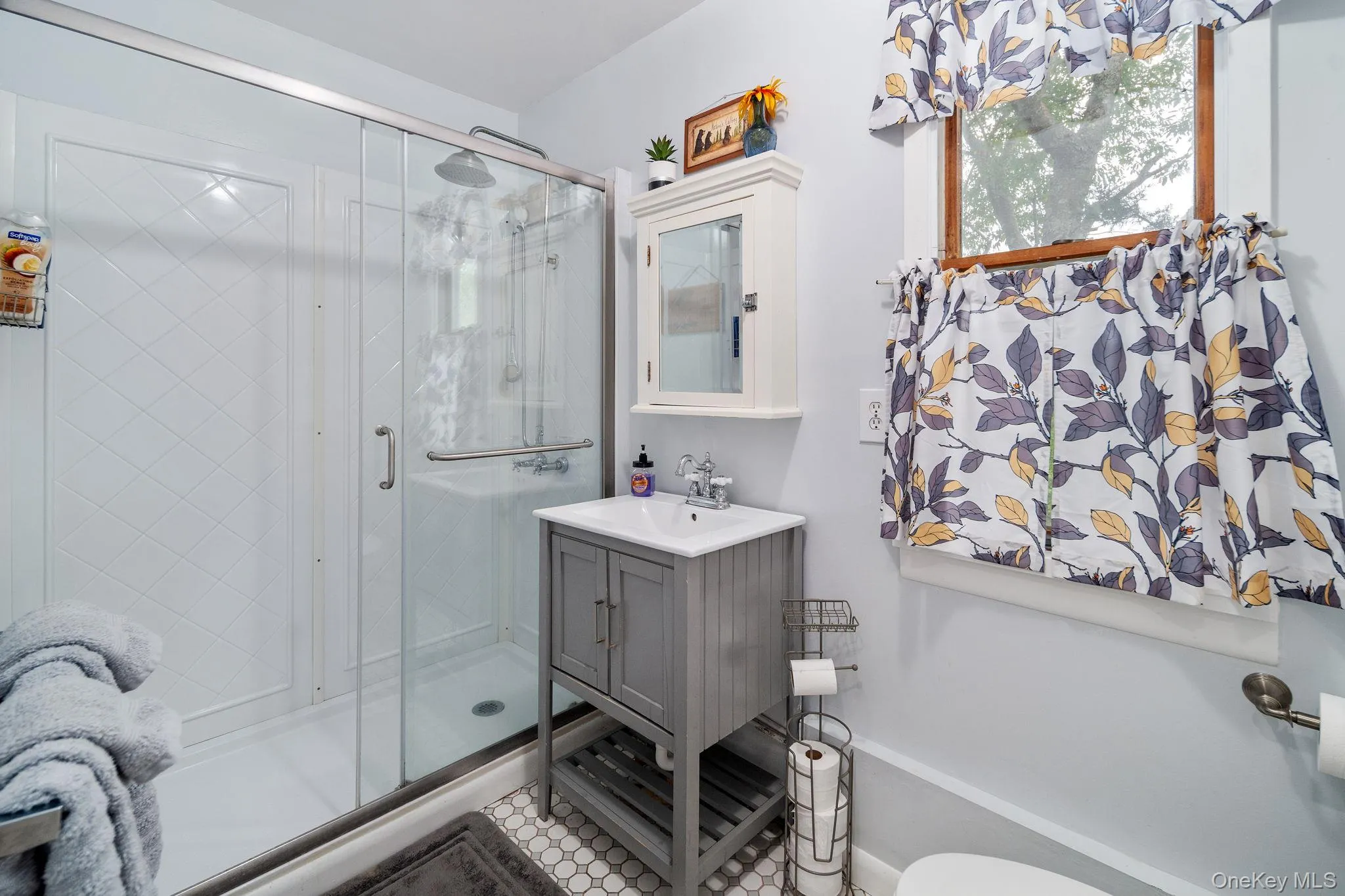Glass-enclosed shower with white tiled surround, single vanity with integrated sink, and hexagon tile flooring Glass-enclosed shower with white tiled surround, single vanity with integrated sink, and hexagon tile flooring